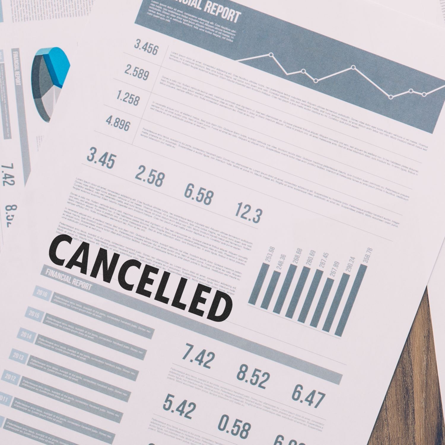 A financial report stamped with CANCELLED using a Large Self Inking Cancelled Stamp, placed on a wooden desk with other documents and charts.