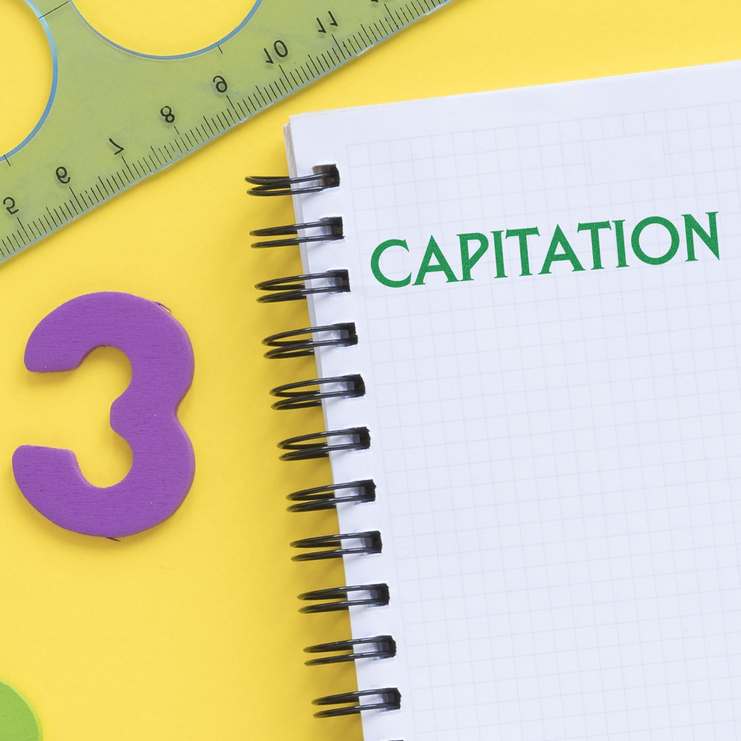 Capitation Rubber Stamp used on a spiral notebook with a green ruler and a purple number 3 on a yellow background.