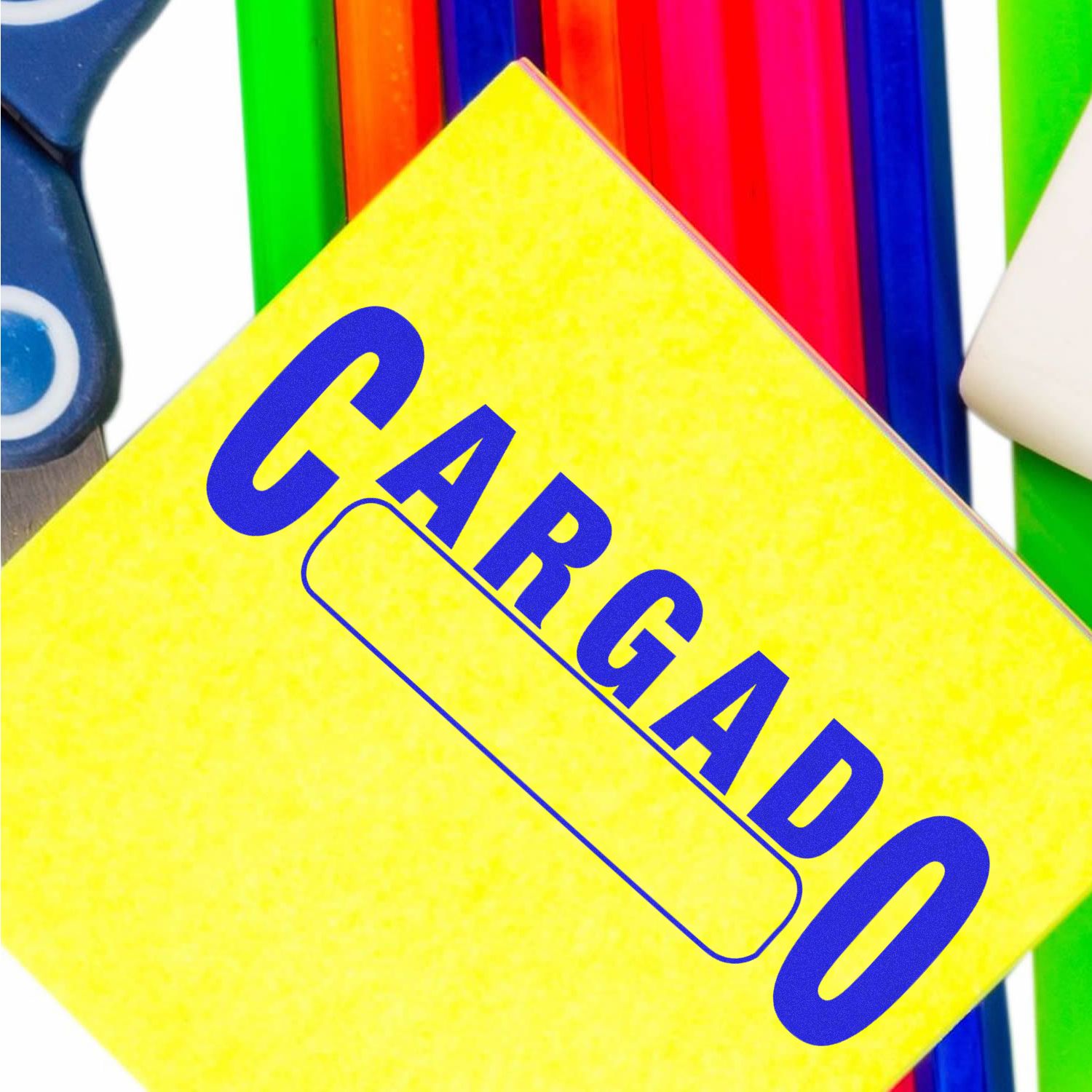 Self Inking Cargado Stamp imprint on a yellow sticky note, surrounded by colorful stationery items including scissors and rulers.