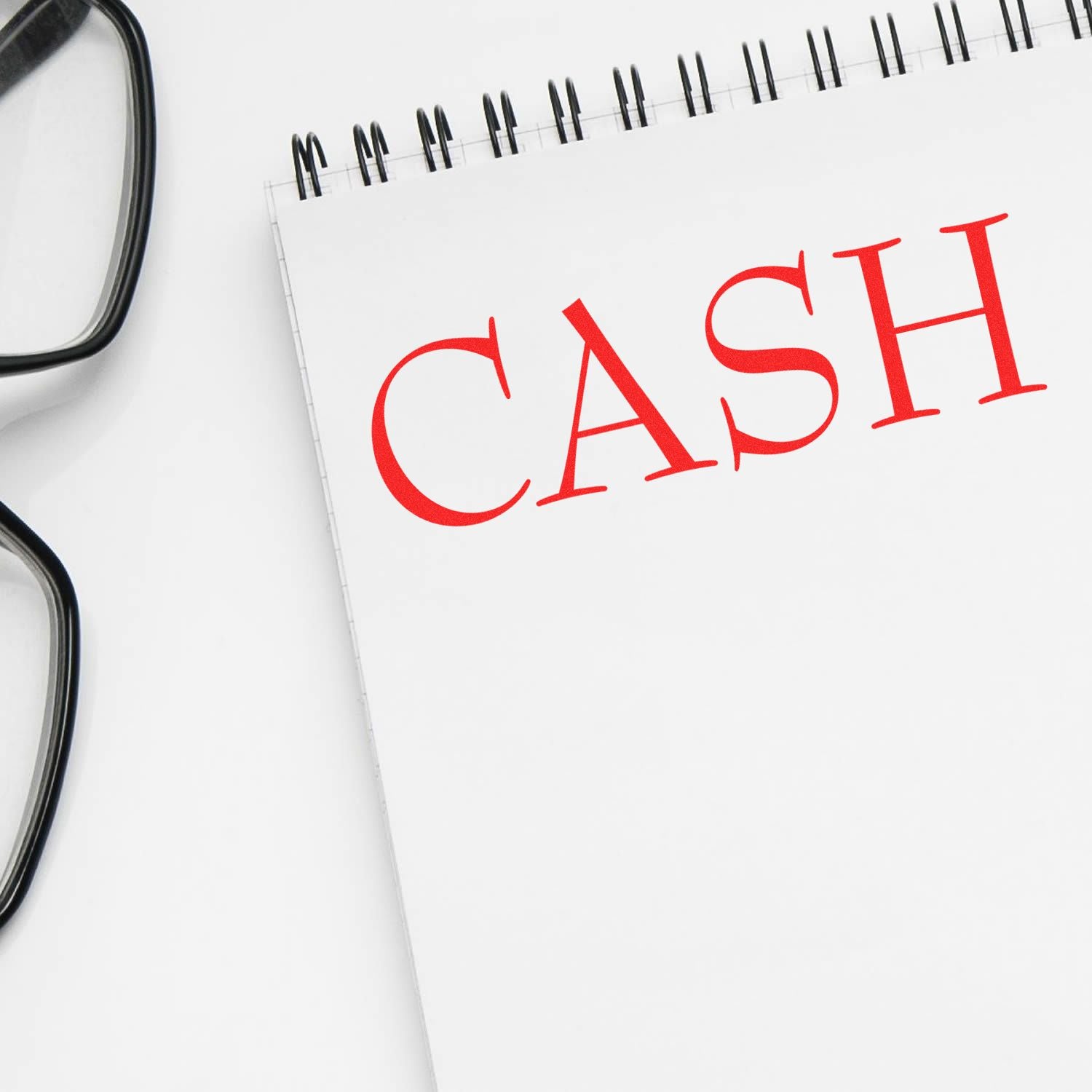 Notebook with a red 'CASH' rubber stamp imprint on a white page, next to a pair of black eyeglasses.