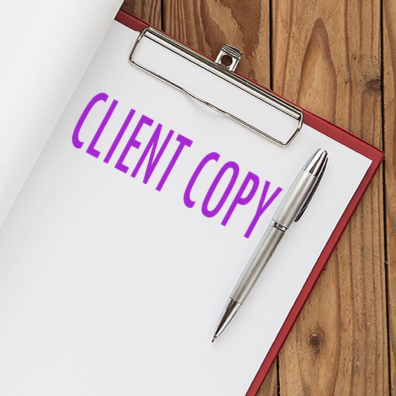 A clipboard with paper stamped CLIENT COPY using a Self Inking Client Copy Stamp, alongside a silver pen on a wooden surface.