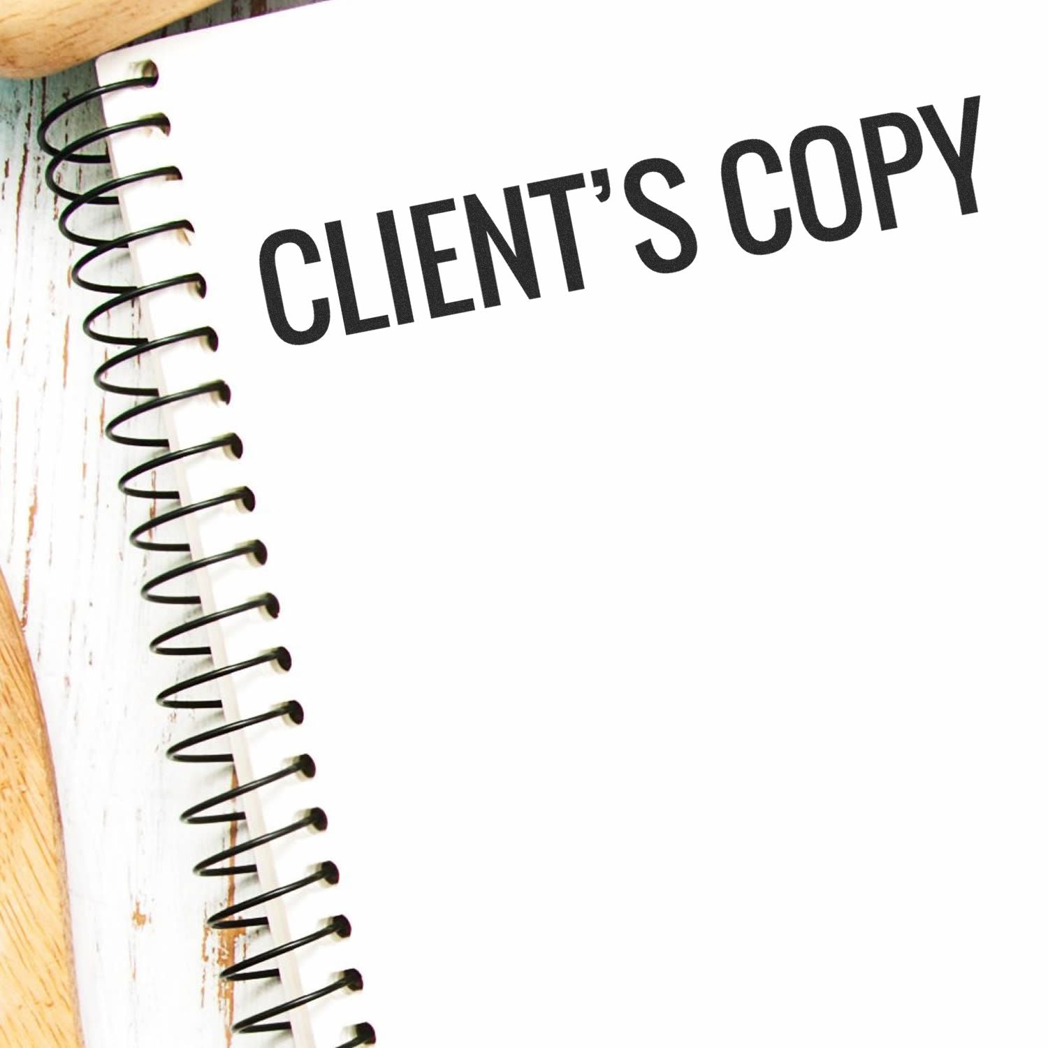 A spiral notebook stamped with CLIENT'S COPY using the Client's Copy Rubber Stamp, placed on a white wooden surface.