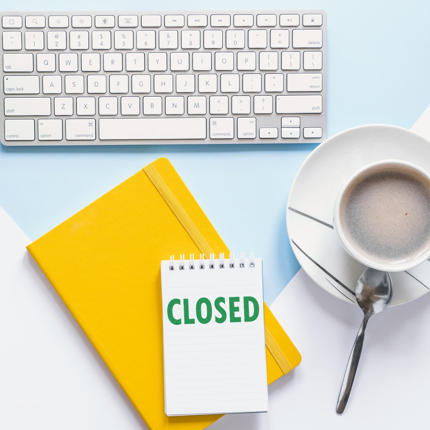 A Closed Rubber Stamp on a notepad, next to a yellow notebook, a cup of coffee, and a white keyboard on a light blue and white background.