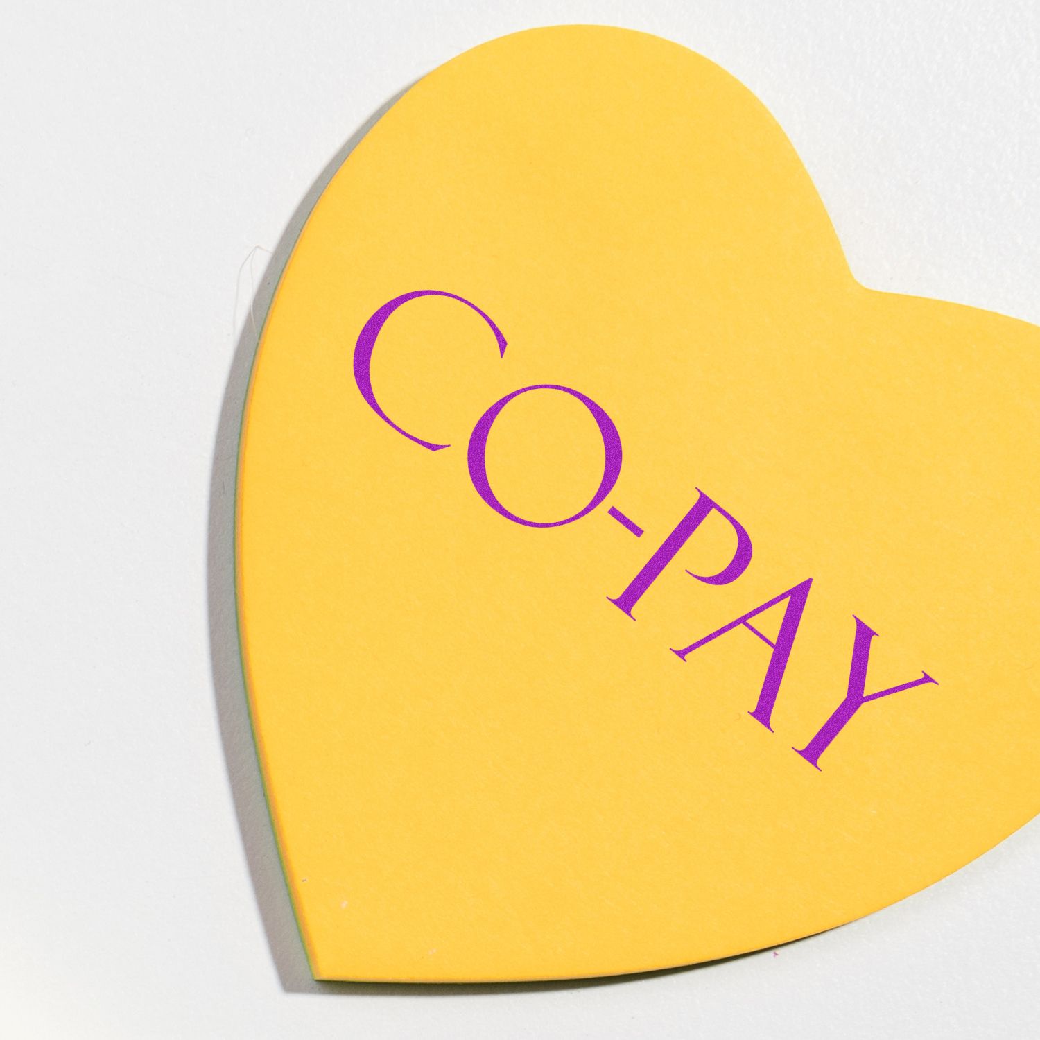 Yellow heart-shaped paper with CO-PAY stamped in purple using the Large Self Inking Co Pay Stamp, placed on a white surface.