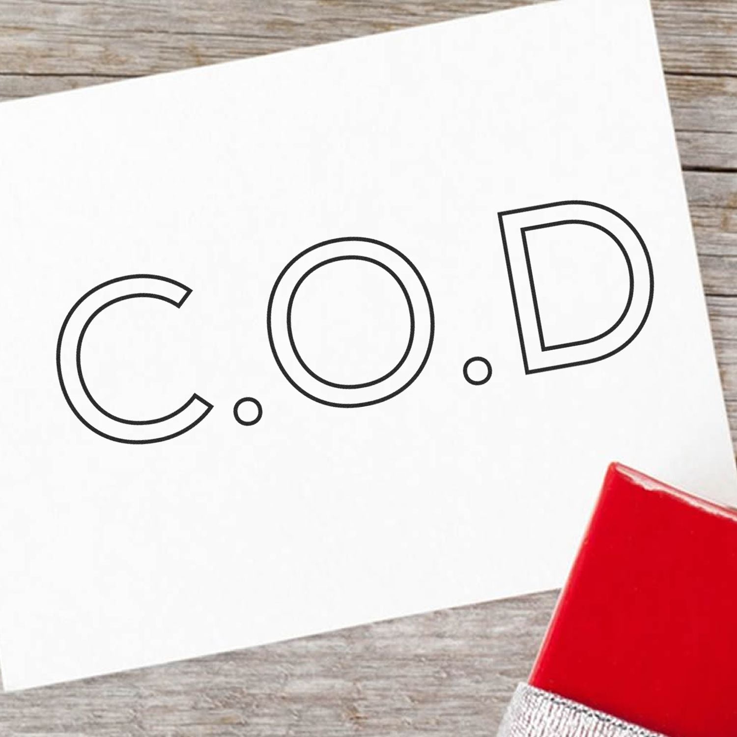 White card stamped with C.O.D using the COD Outline Rubber Stamp, placed on a wooden surface with a red stamp pad in the corner.