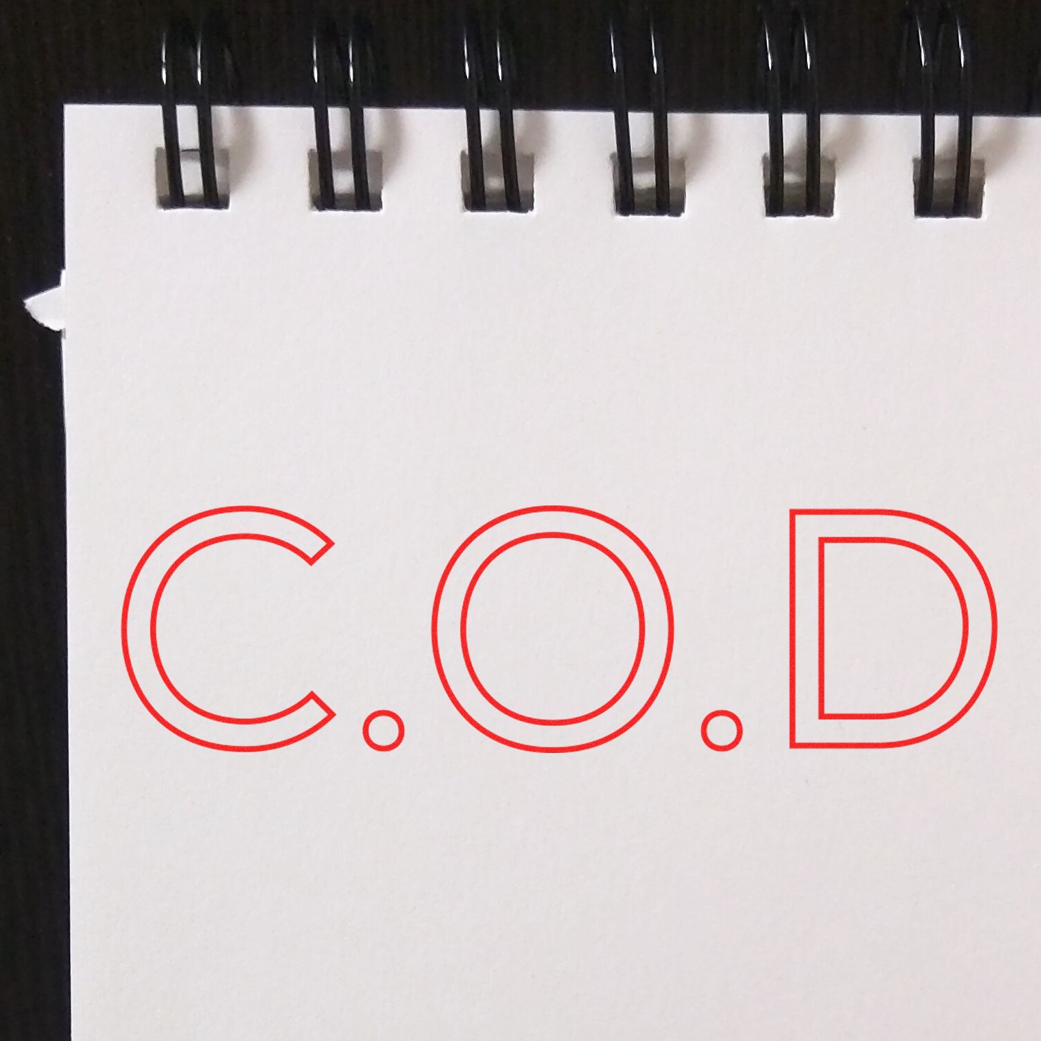 A notebook with a spiral binding displays the text C.O.D in red, stamped using the COD Outline Rubber Stamp.