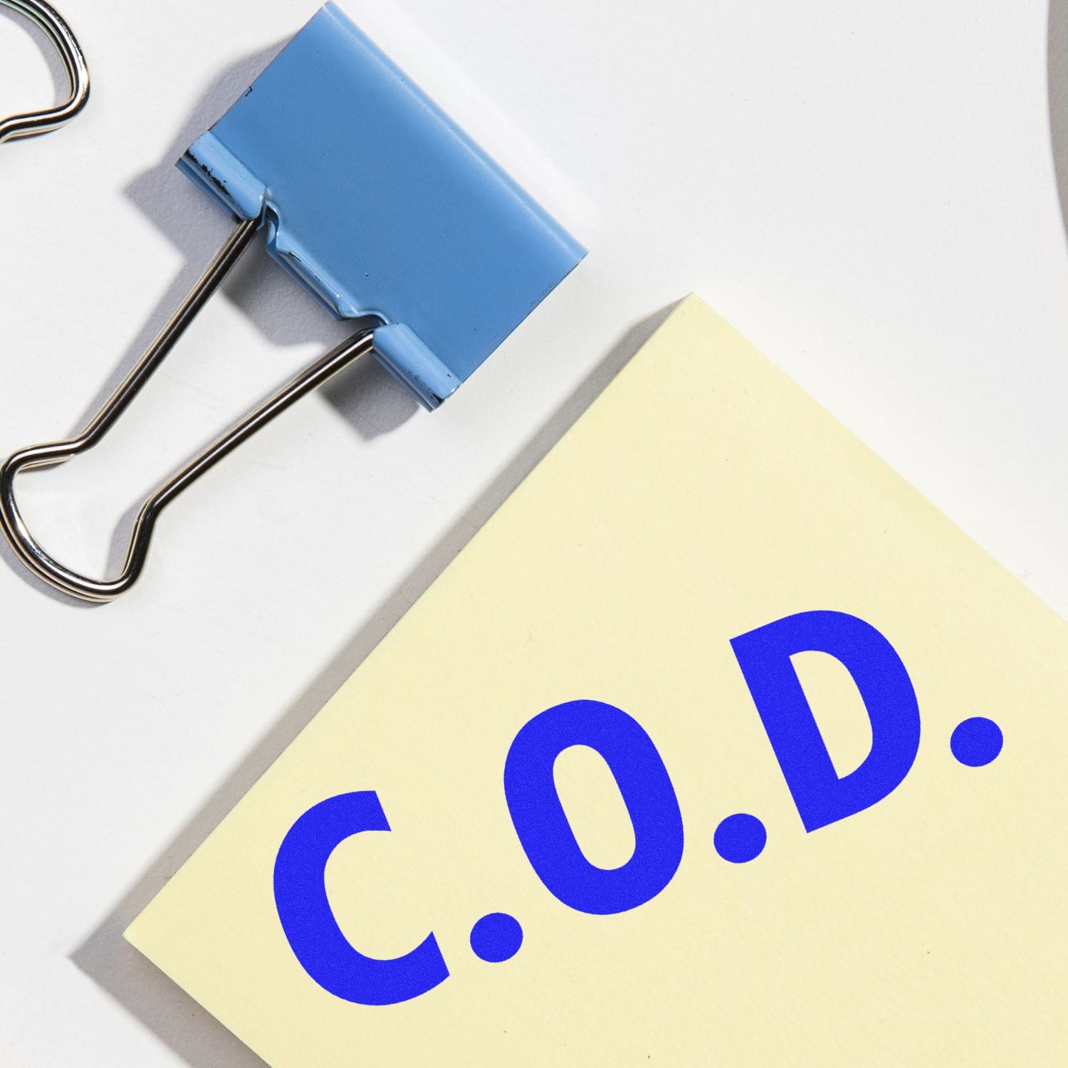 Large COD Rubber Stamp imprint on a yellow paper next to a blue binder clip on a white surface.