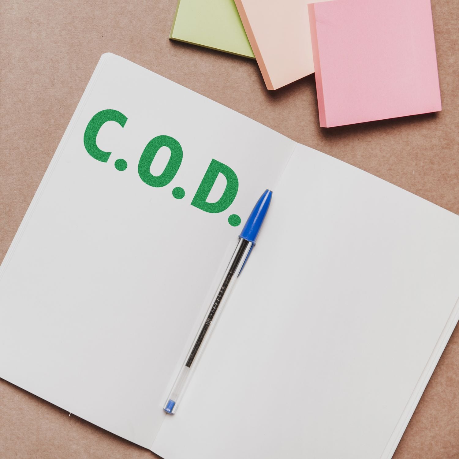 Large Self Inking COD Office Stamp in use, stamping C.O.D. in green ink on an open notebook with a blue pen and colorful sticky notes nearby.