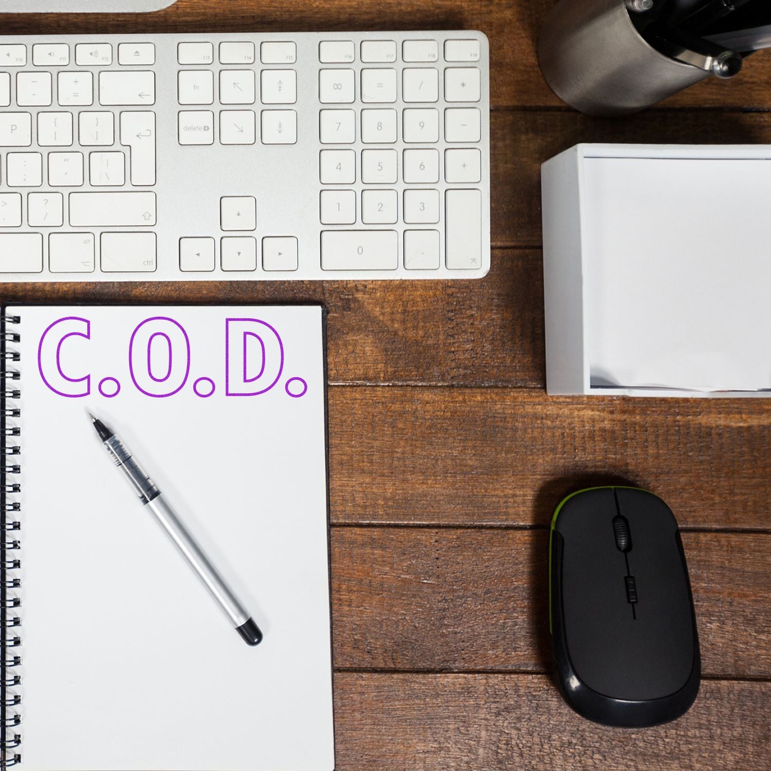 A desk with a keyboard, mouse, pen, and notebook stamped with C.O.D. using the COD With Outline Text Rubber Stamp.