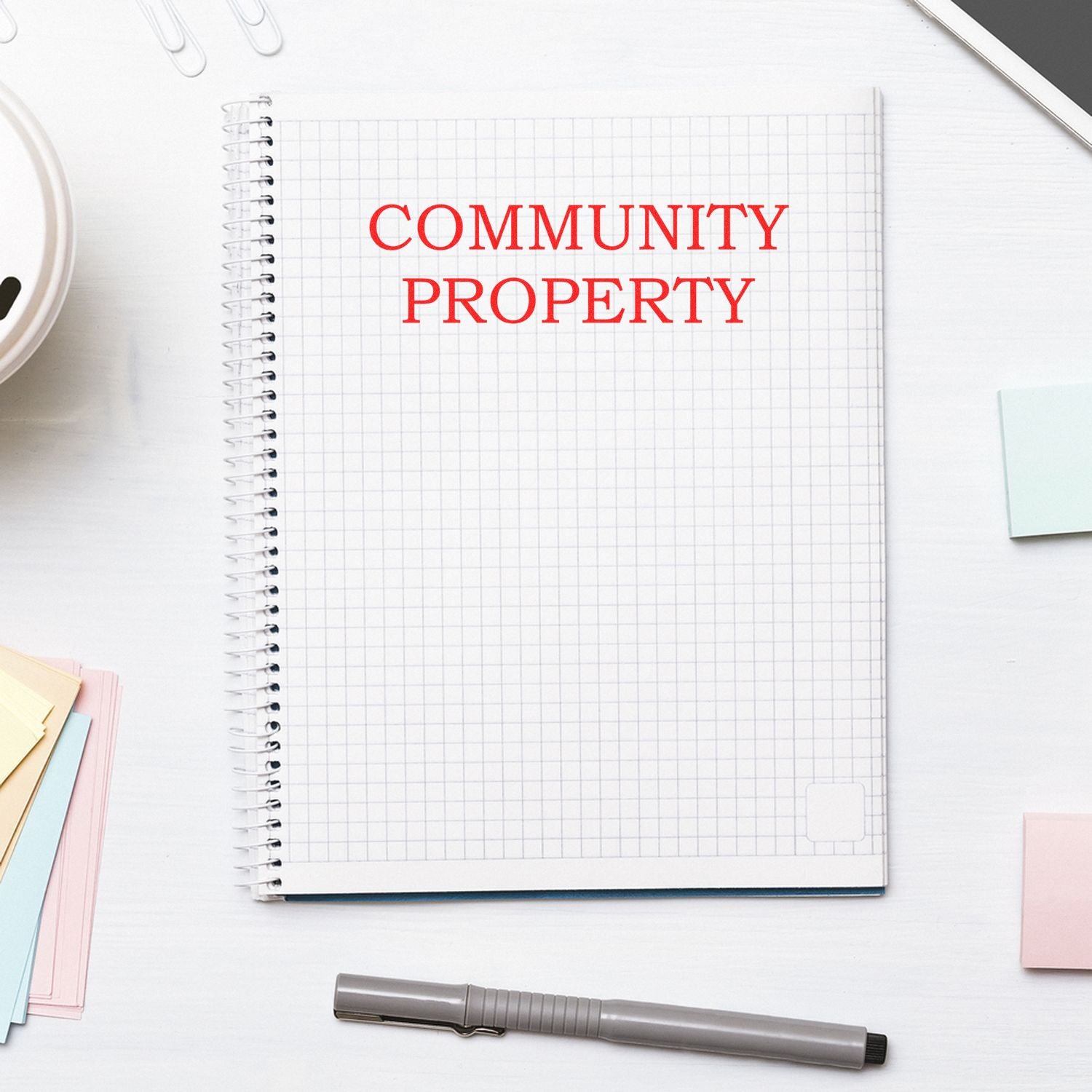 Slim Pre-Inked Community Property Stamp used on a spiral notebook with grid paper, surrounded by office supplies.