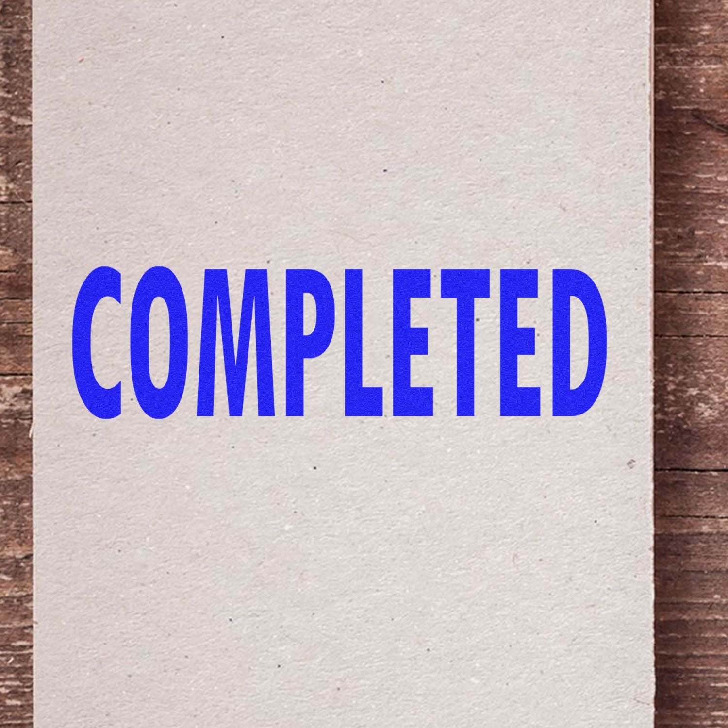 A piece of paper stamped with the word 'COMPLETED' in blue ink using the Completed Rubber Stamp, placed on a wooden surface."