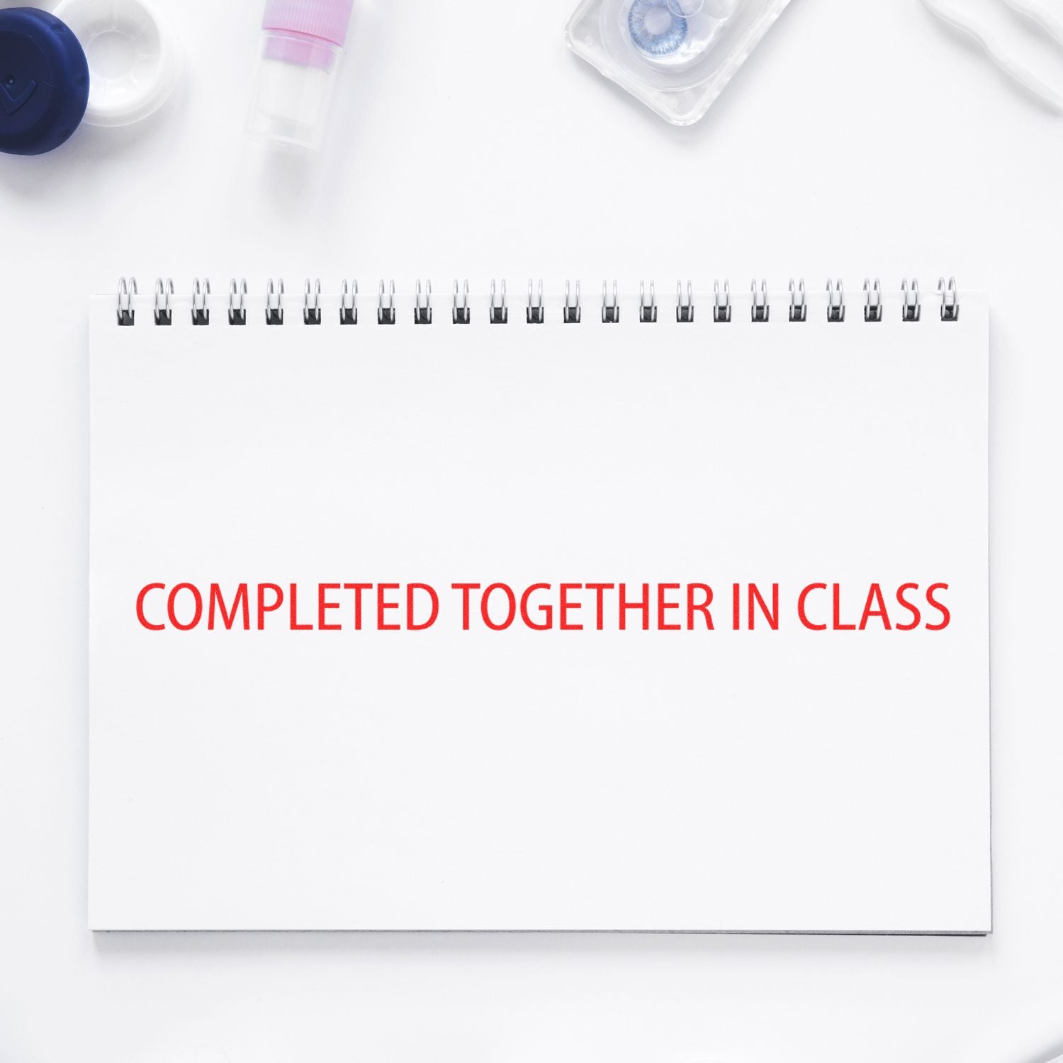 A notebook with the text 'COMPLETED TOGETHER IN CLASS' stamped in red using the Large Self Inking Completed Together Stamp, surrounded by various stationery items on a white background.