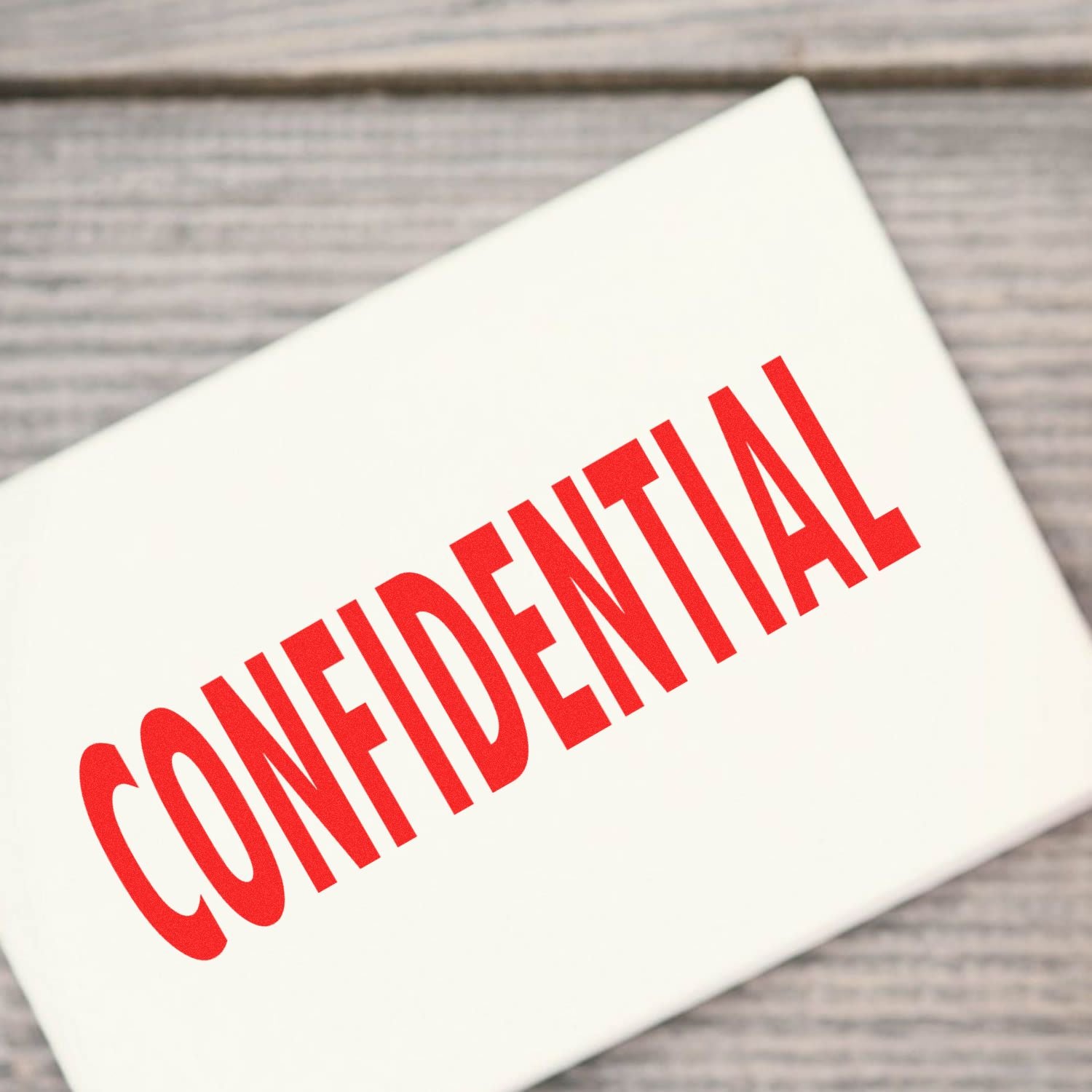 Large Confidential Rubber Stamp imprinting the word CONFIDENTIAL in bold red letters on a white surface, placed on a wooden background.