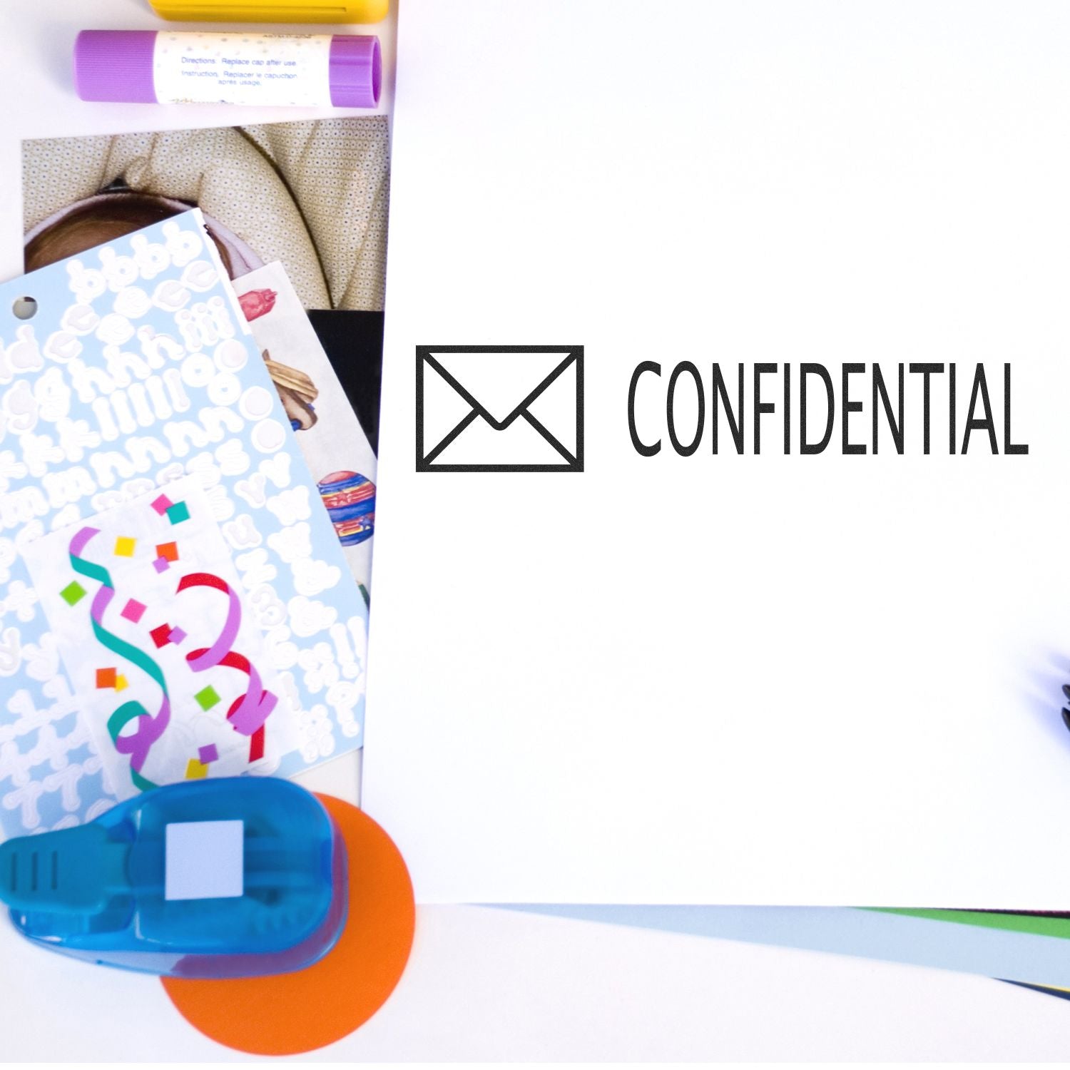 Large Self Inking Confidential with Envelope Stamp used on a white paper, surrounded by colorful stationery items including stickers, a glue stick, and a blue tape dispenser.