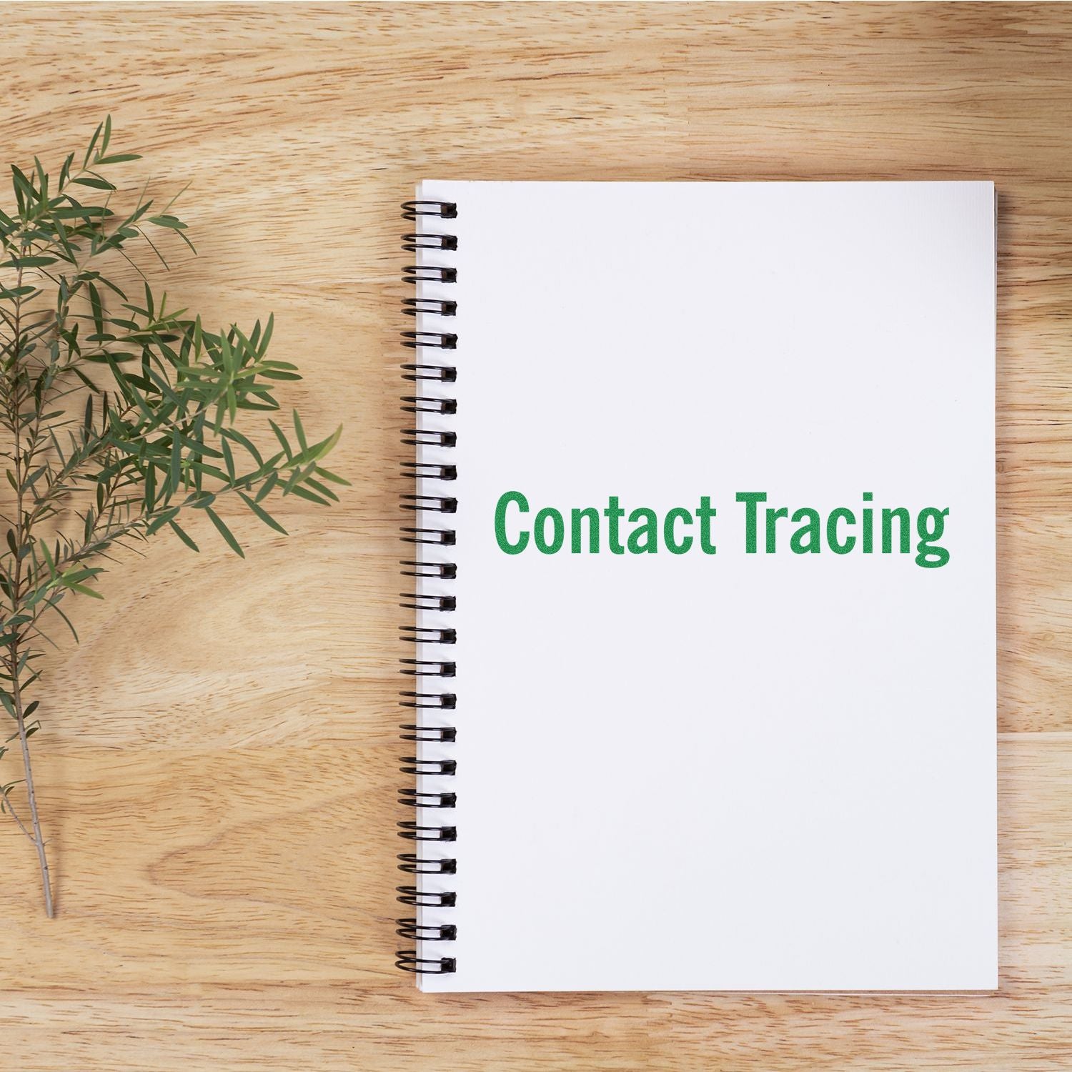 A notebook stamped with Contact Tracing using the Large Pre-Inked Contact Tracing Stamp, placed on a wooden surface next to a sprig of greenery.