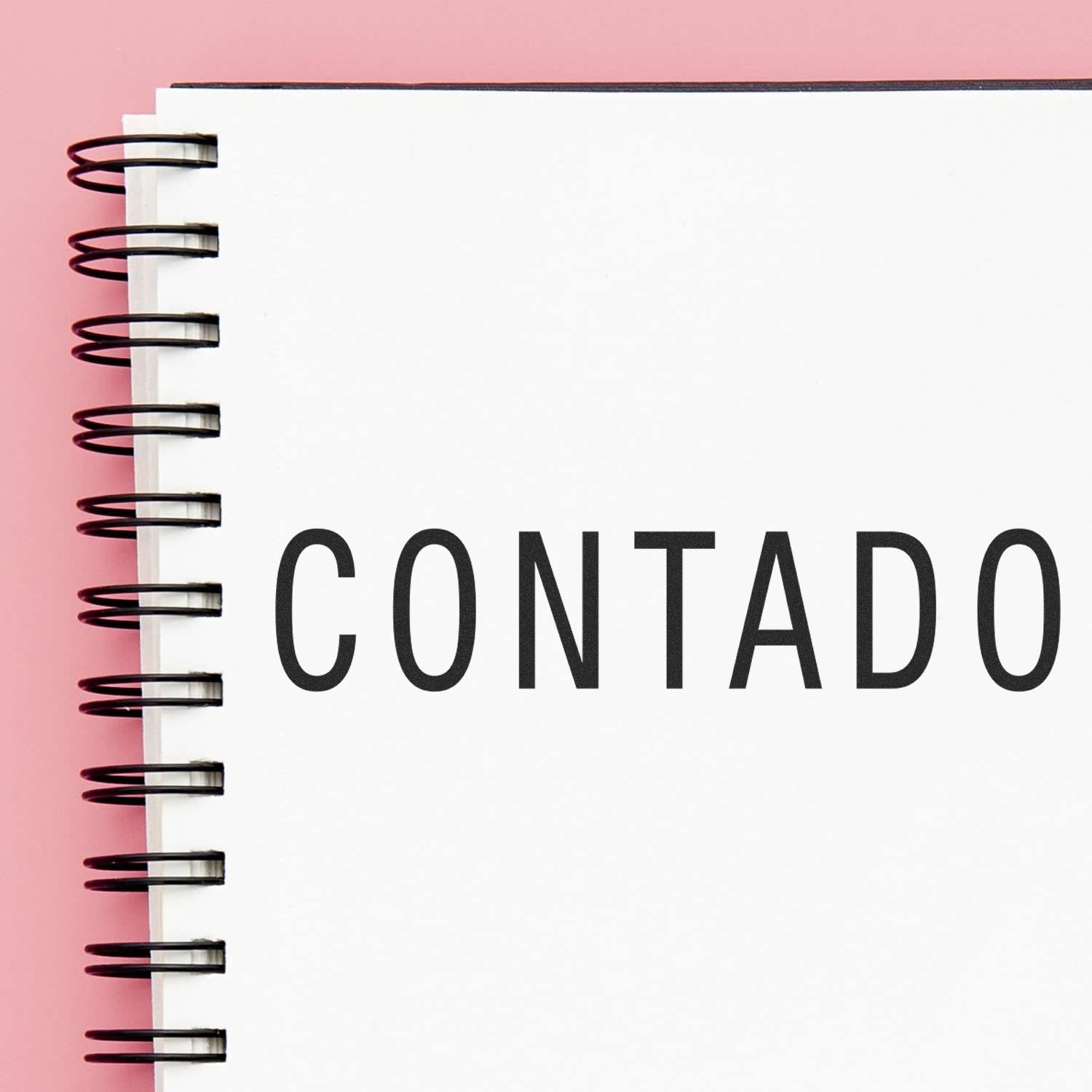 A Large Pre-Inked Contado Stamp imprint on a white spiral notebook page with a pink background.