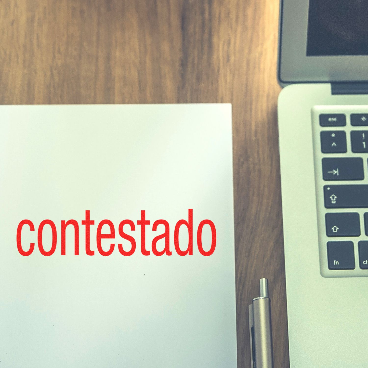 Large Contestado Rubber Stamp in use, stamping the word contestado in red on white paper, next to a silver pen and a laptop on a wooden desk.