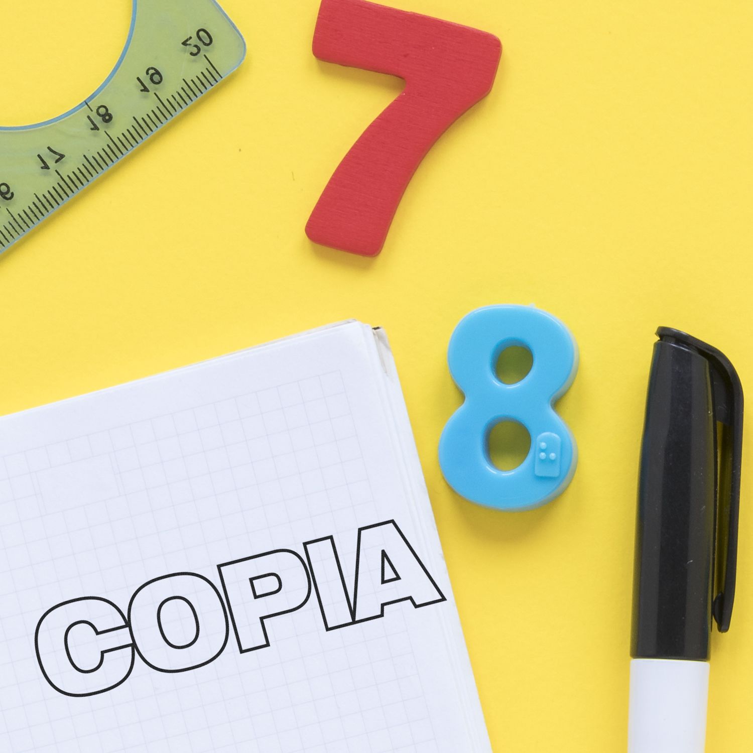 Large Copia Rubber Stamp in use on a notebook, surrounded by a ruler, red number 7, blue number 8, and a black pen on a yellow background.