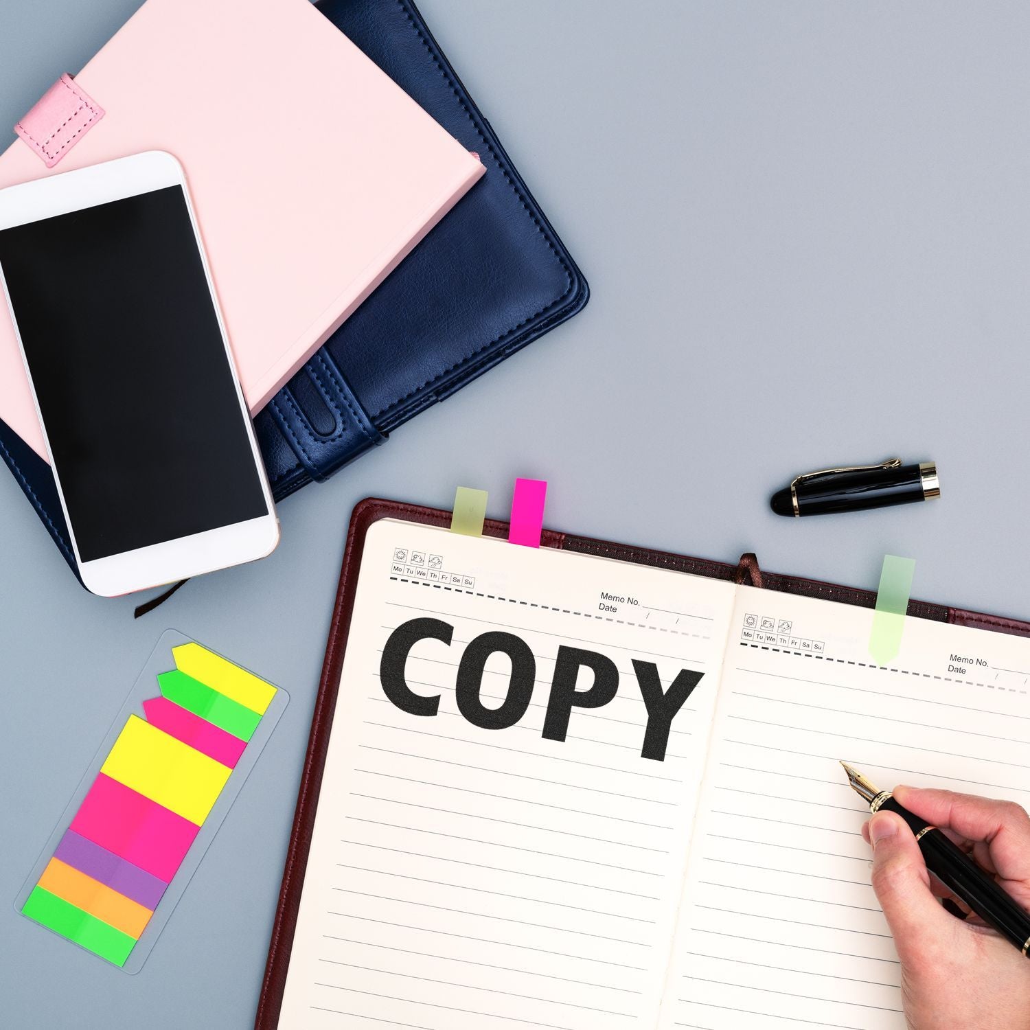 A desk with a Copy Rubber Stamp used on a notebook, surrounded by a smartphone, colorful sticky notes, and a pen.