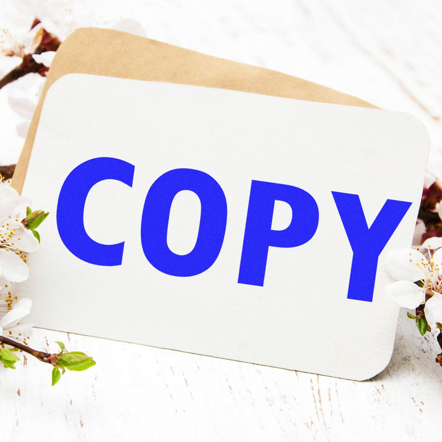 A Copy Rubber Stamp imprint on a white card with blue text COPY, placed on a wooden surface with flowers in the background.