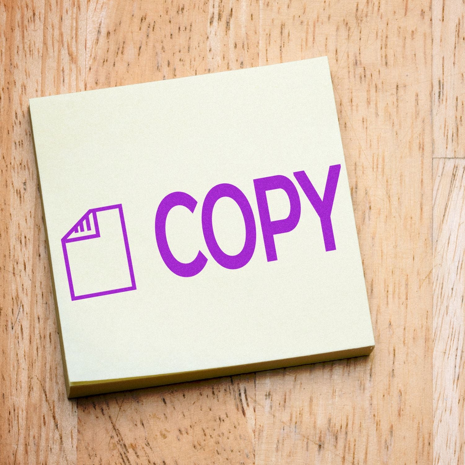 Self Inking Copy with Letter Stamp imprinting the word COPY in purple on a yellow sticky note on a wooden surface.