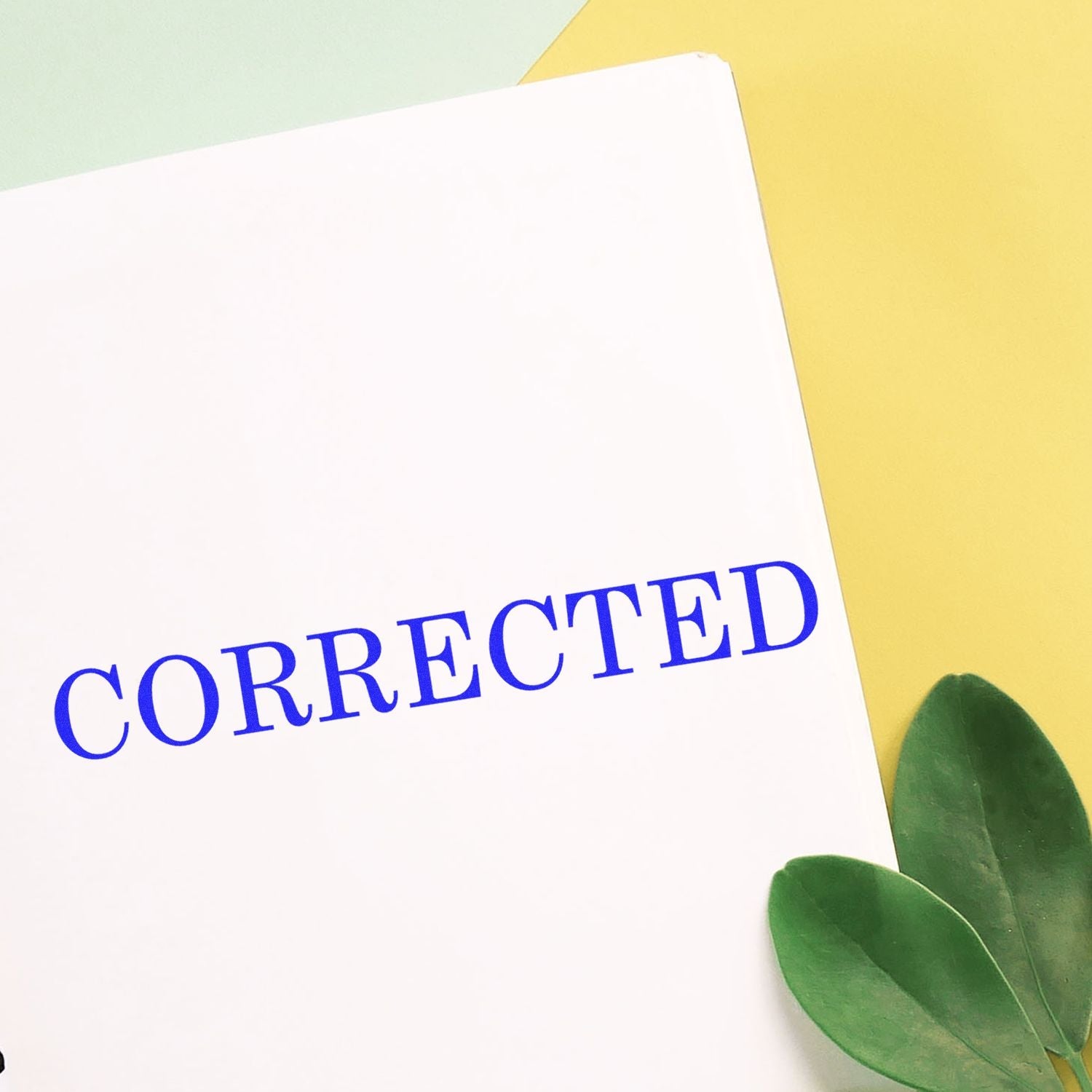 Self Inking Corrected Stamp in blue ink on white paper, with green leaves and yellow background.