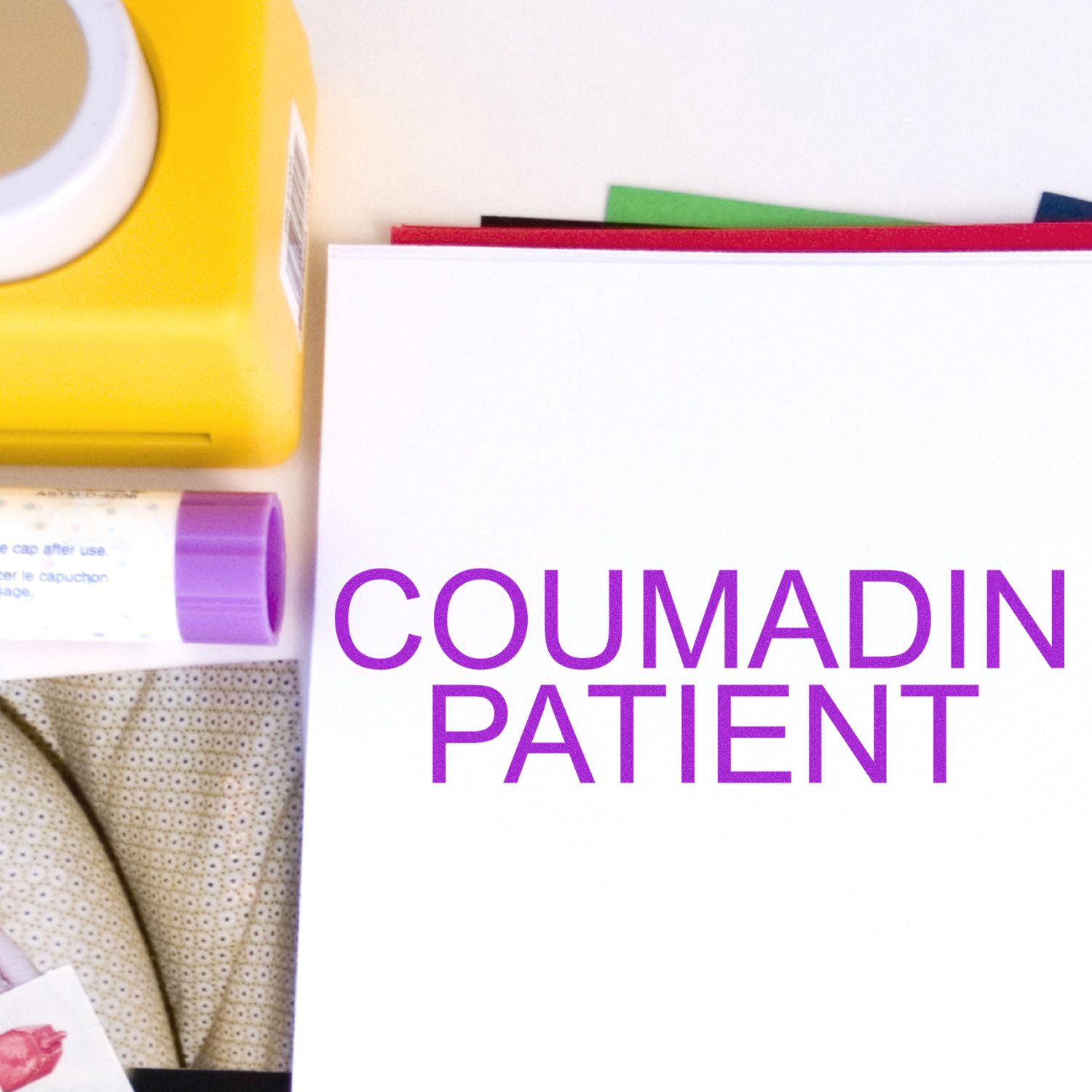 Coumadin Patient Rubber Stamp in use, stamping COUMADIN PATIENT in purple ink on white paper, with other office supplies nearby.