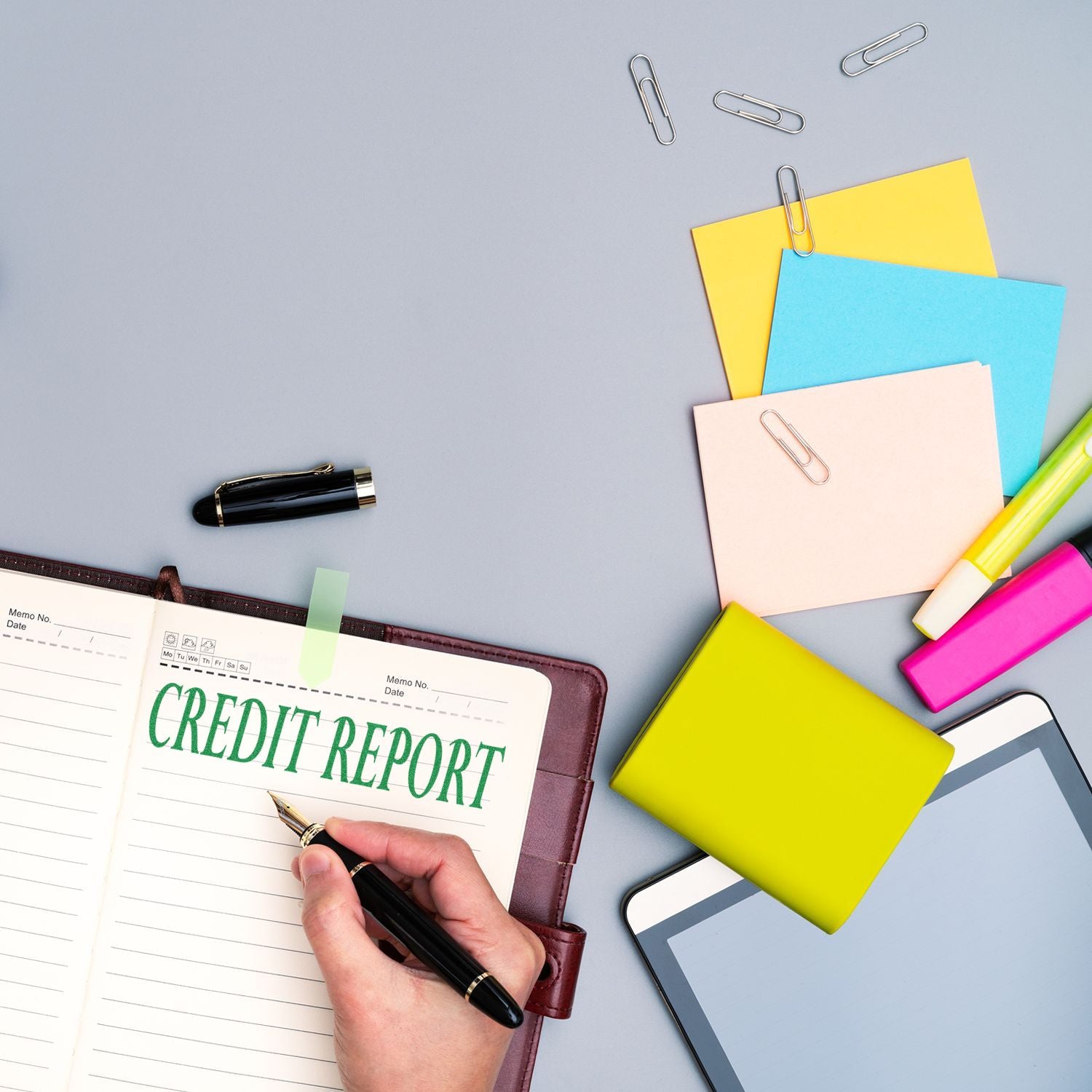 Person using a Slim Pre-Inked Credit Report Stamp on a notebook, surrounded by office supplies like pens, sticky notes, and a tablet.