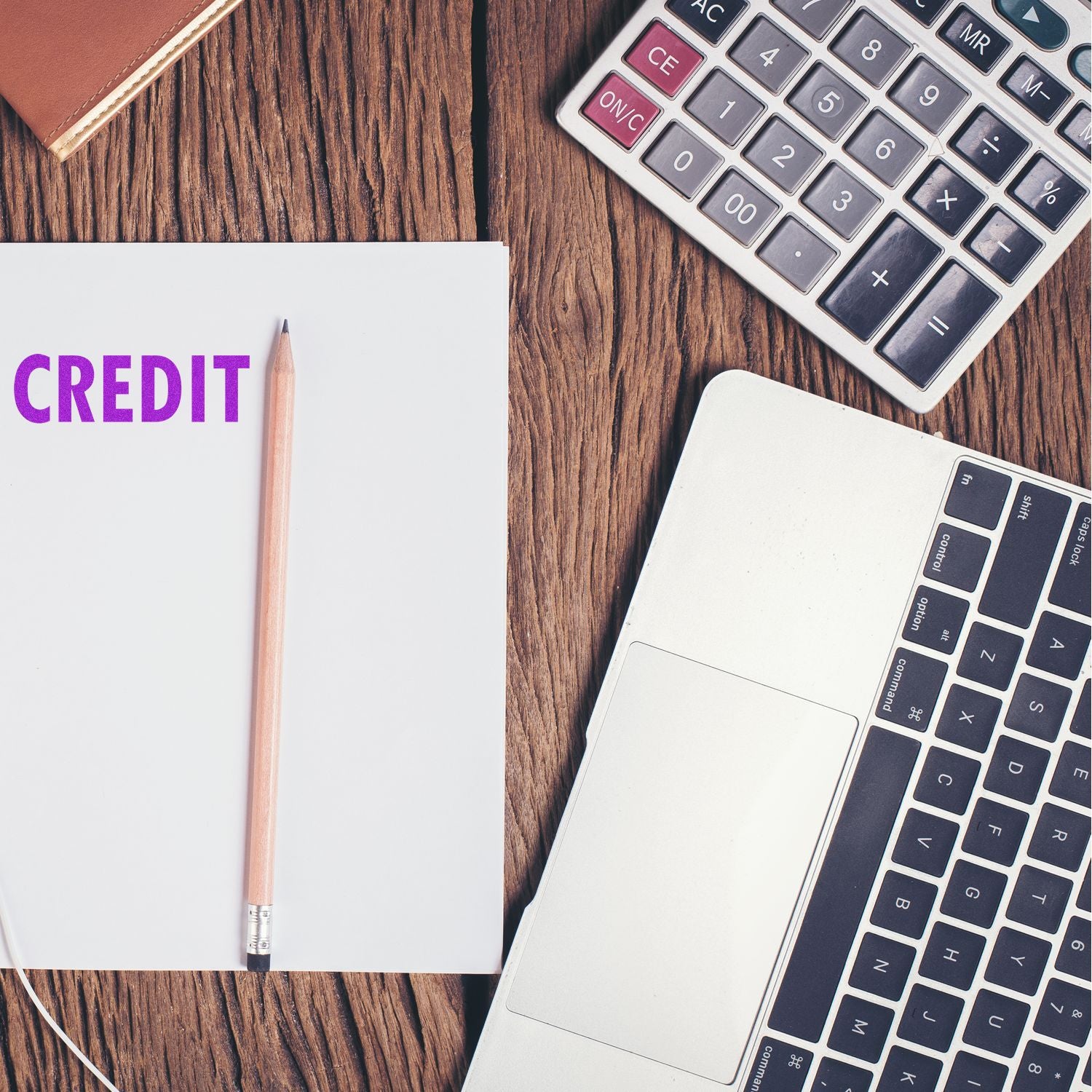 A Large Black Credit Rubber Stamp is used on a white paper with CREDIT in purple, next to a pencil, laptop, and calculator on a wooden desk.