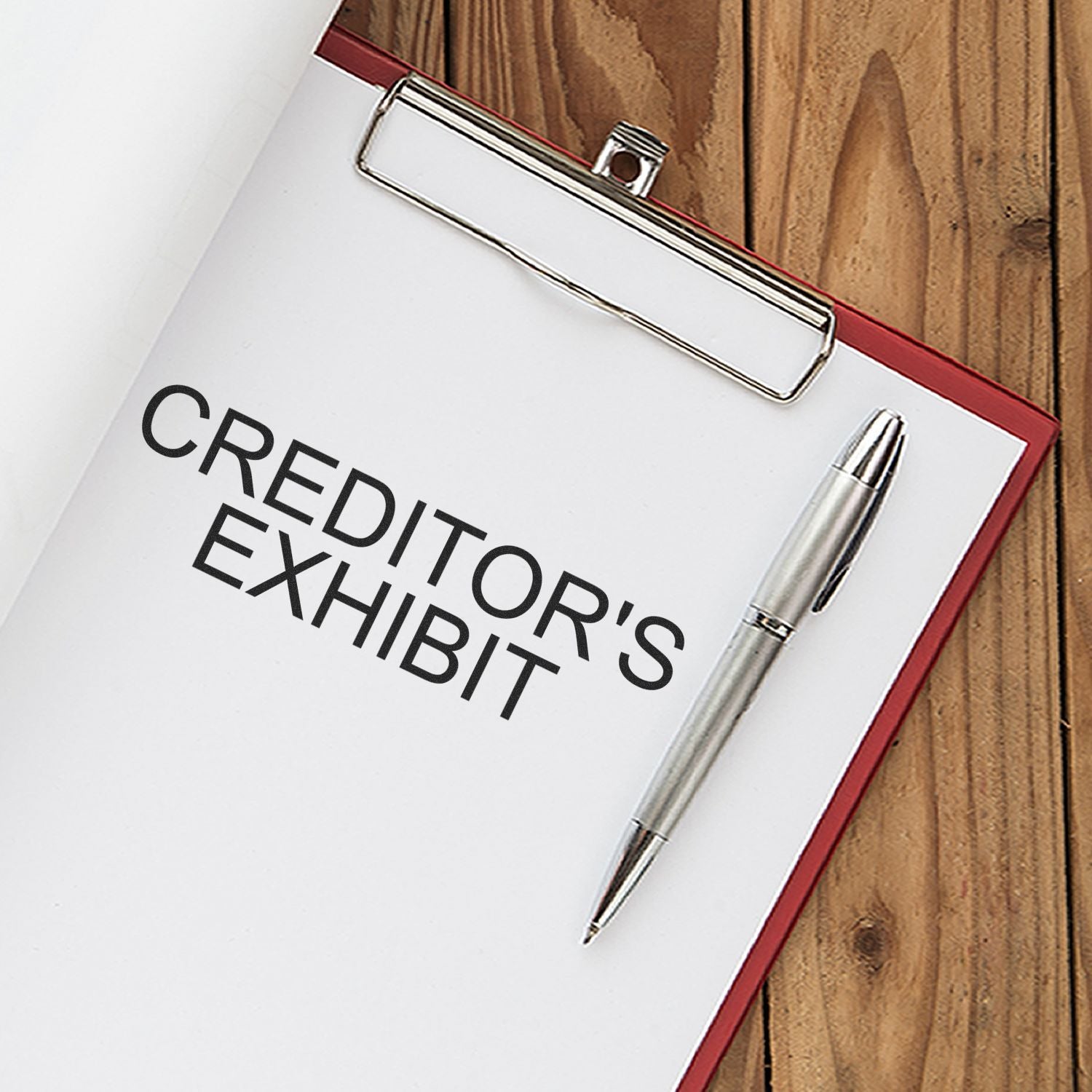 Clipboard with a stamped document reading CREDITOR'S EXHIBIT using the Self Inking Creditors Exhibit Stamp, alongside a silver pen on a wooden surface.