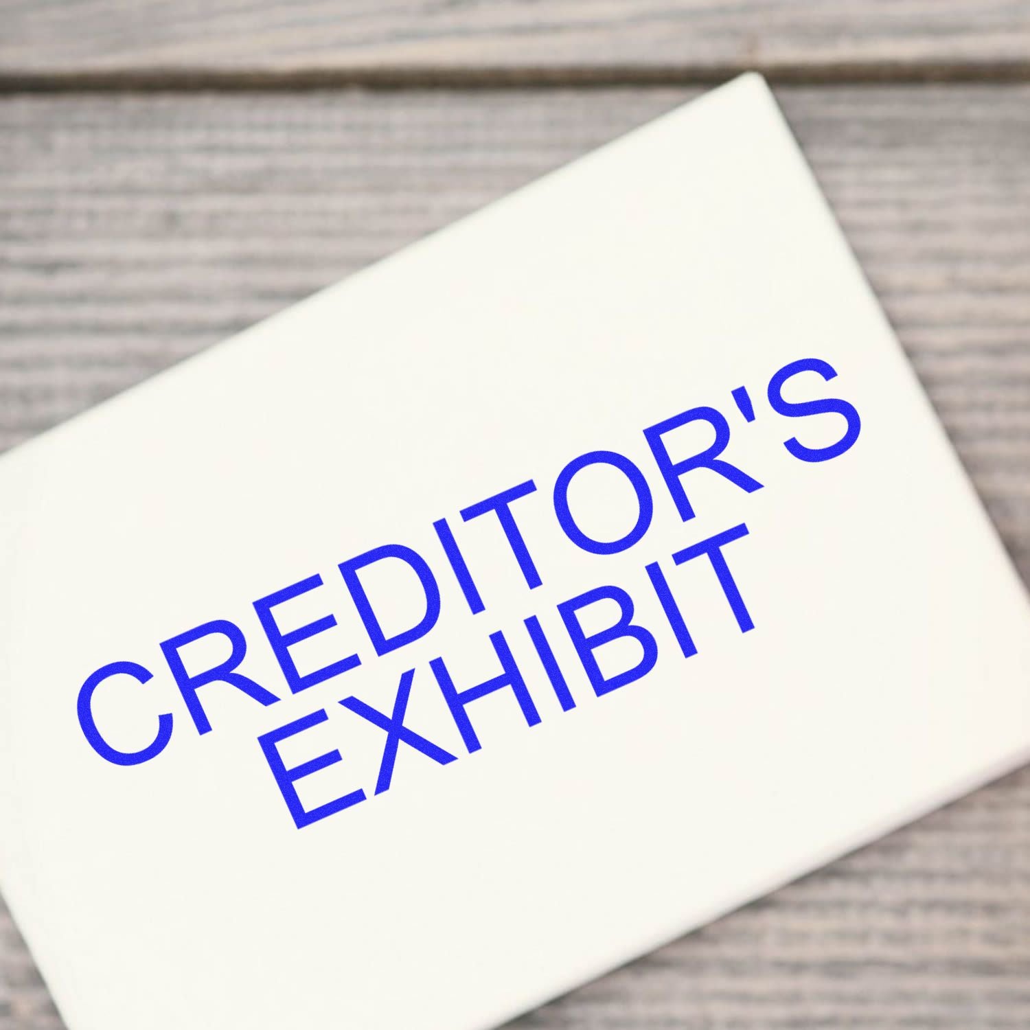 Self Inking Creditors Exhibit Stamp in blue ink on a white surface, placed on a wooden background.