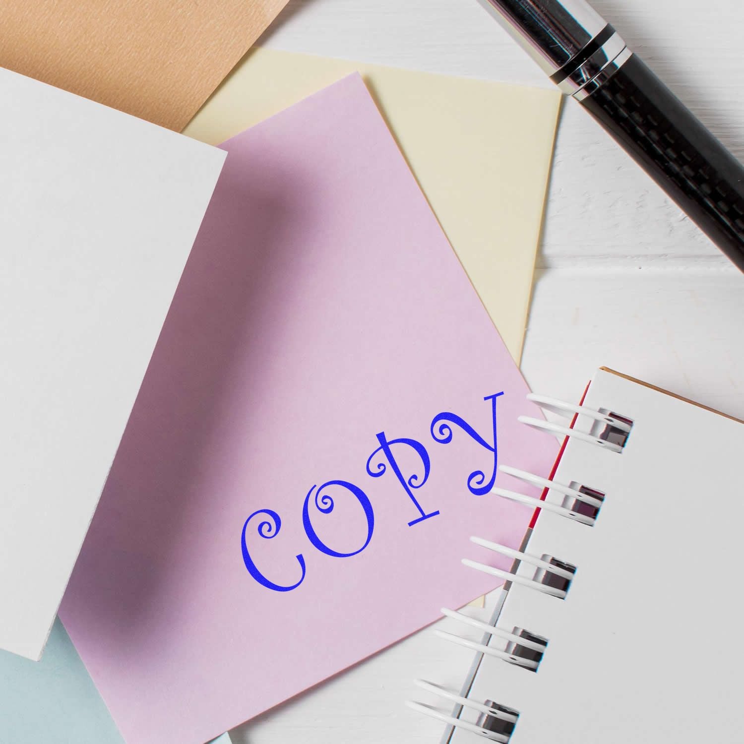 Large Self Inking Curly Copy Stamp marking COPY in blue on a pink paper, surrounded by other papers and a pen.