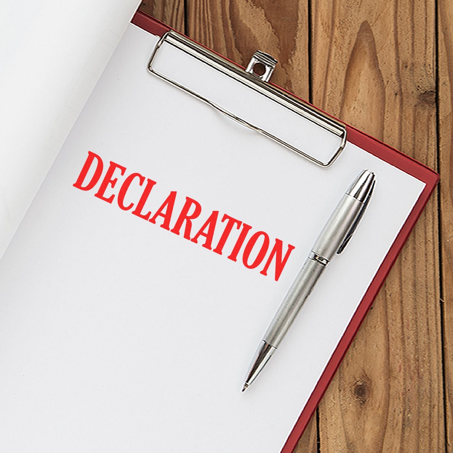 Slim Pre-Inked Declaration Stamp in red ink on a white paper clipped to a clipboard with a silver pen on a wooden surface.