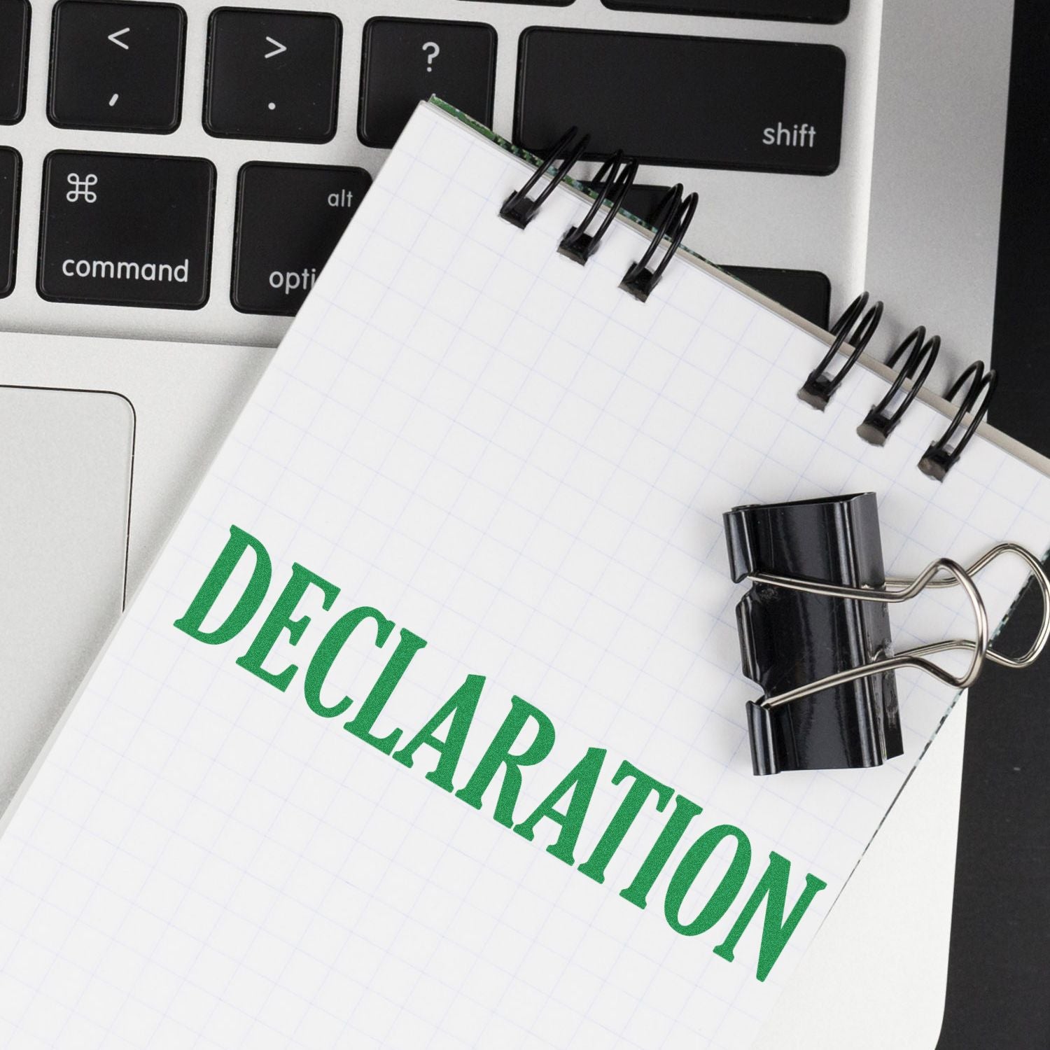 Large Declaration Rubber Stamp used on a notepad with the word DECLARATION in green, placed on a laptop keyboard with a binder clip.