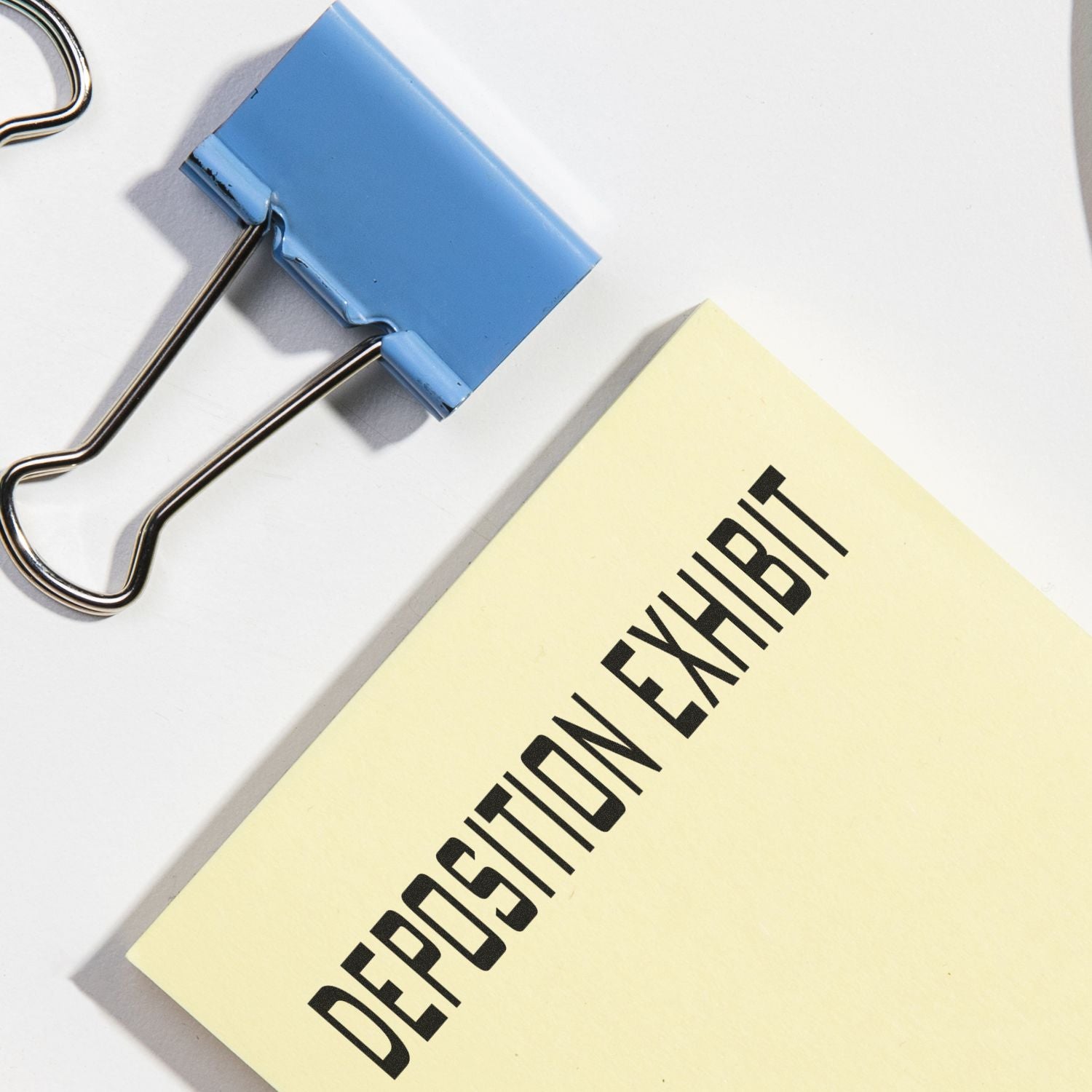 Self Inking Deposition Exhibit Stamp marking a yellow document, next to a blue binder clip on a white surface.