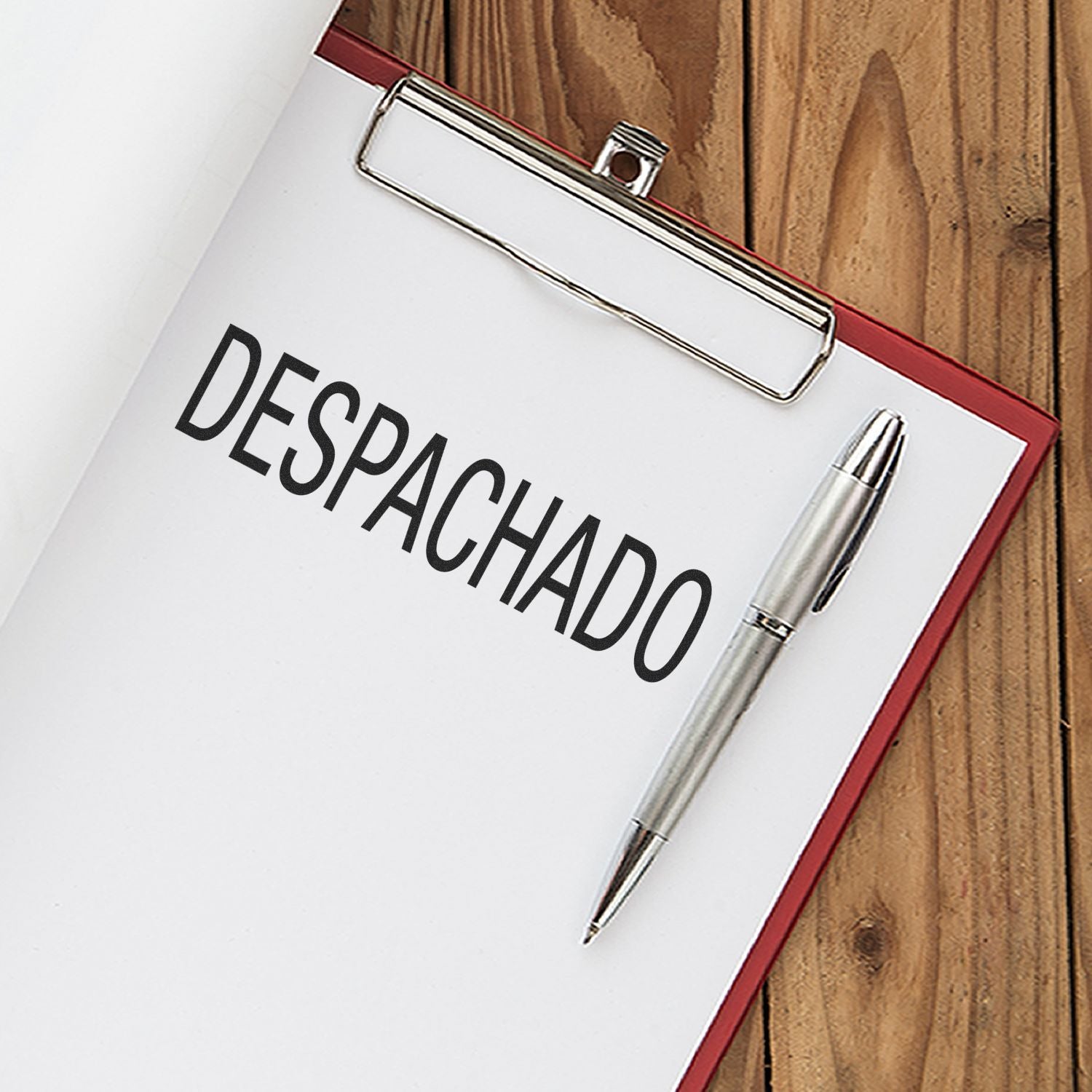 Clipboard with paper stamped "DESPACHADO" using the Slim Pre-Inked Despachado Stamp, alongside a silver pen on a wooden surface.