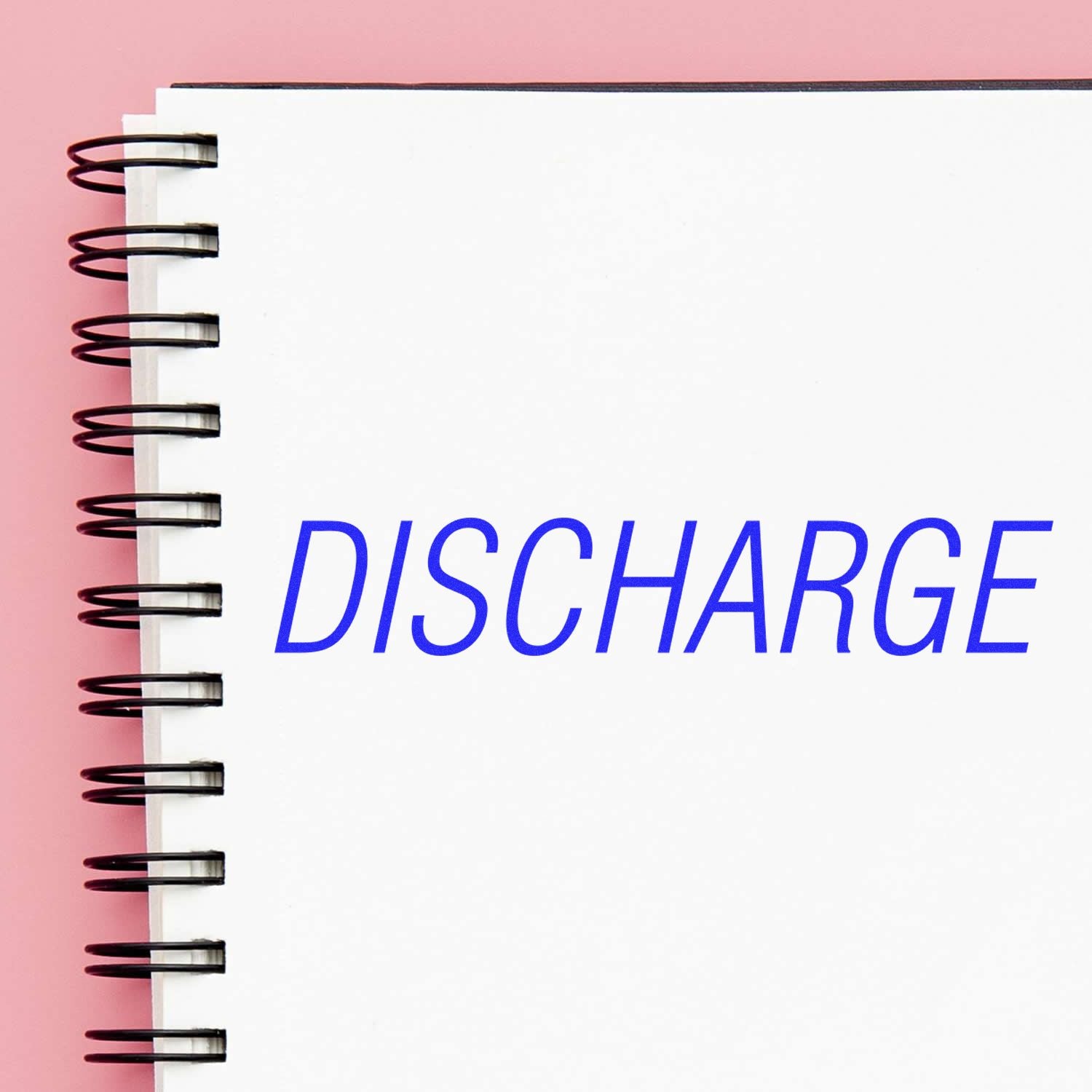 A notebook with a spiral binding and a white page stamped with the word DISCHARGE in blue using the Discharge Rubber Stamp.