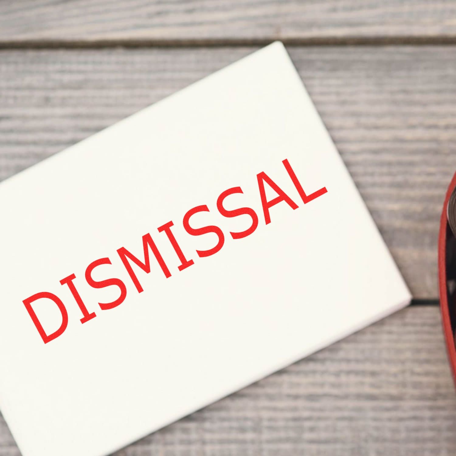 Large Dismissal Rubber Stamp in use, stamping the word DISMISSAL in red ink on a white paper, placed on a wooden surface.