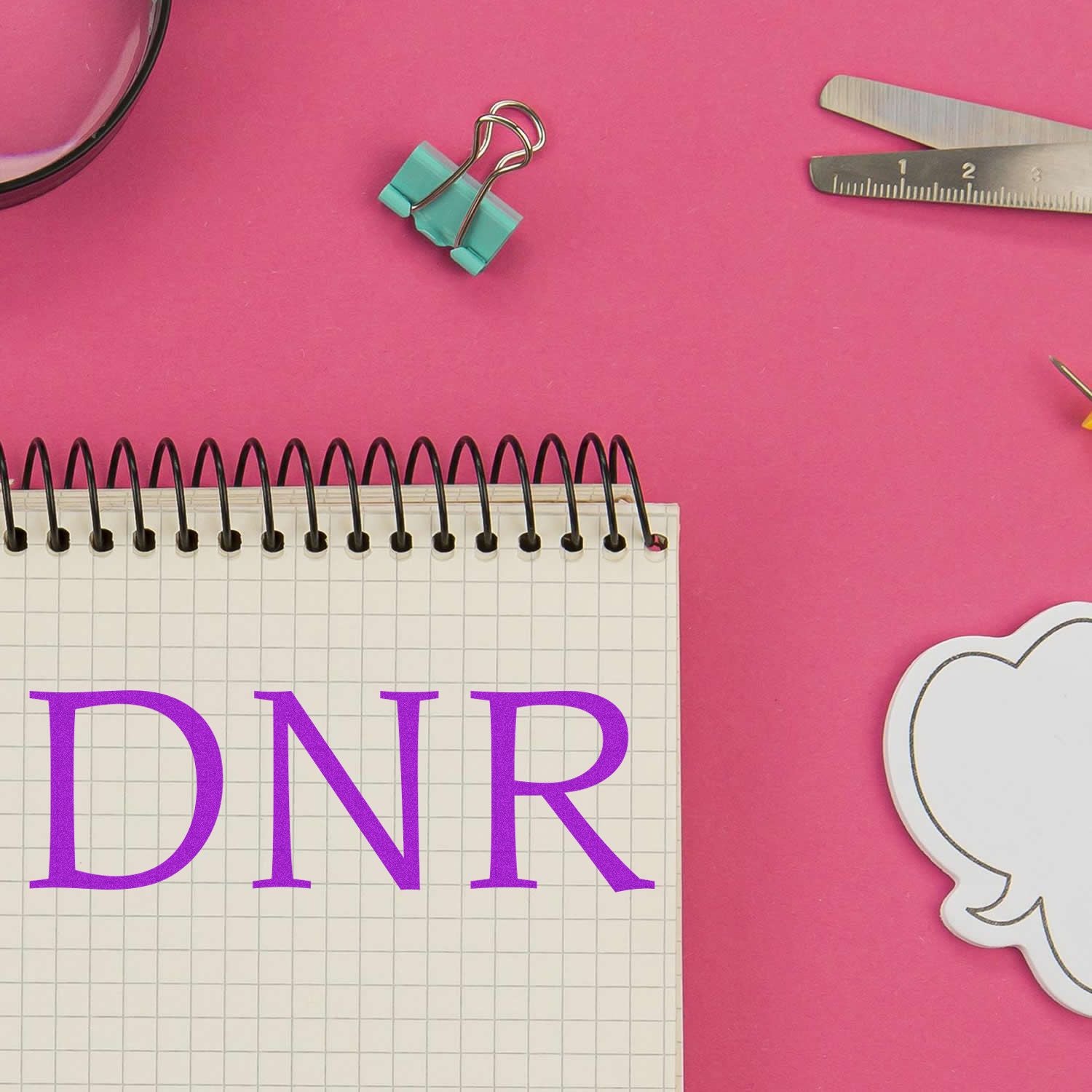 Slim Pre-Inked DNR Stamp used on a notebook with a pink background, surrounded by office supplies like rulers and clips.