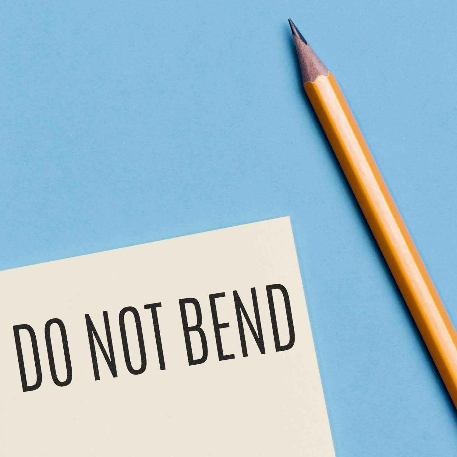 Slim Pre-Inked Do Not Bend Stamp on a white envelope next to a yellow pencil on a blue background.