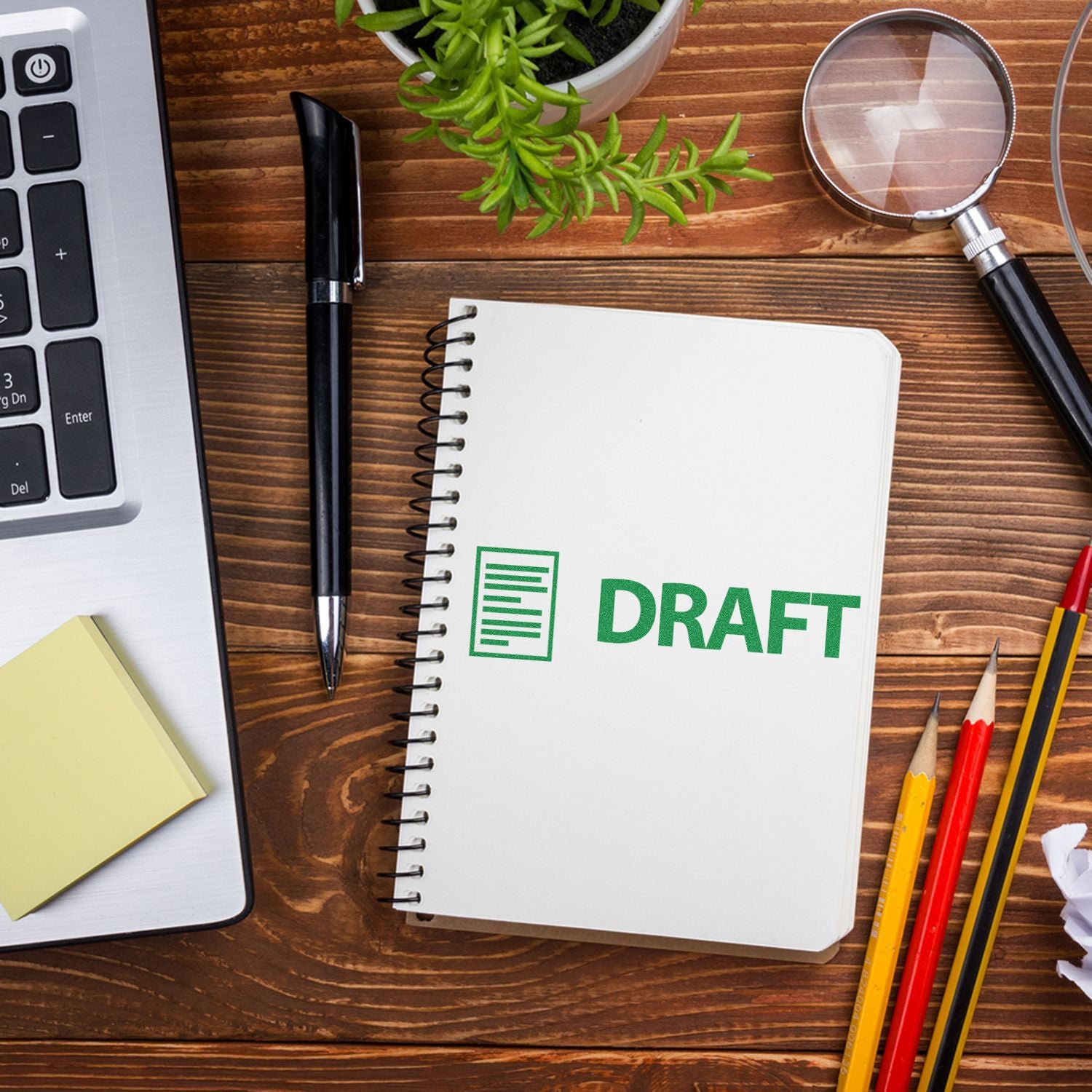 Large Self Inking Draft with Letter Stamp used on a spiral notebook, placed on a wooden desk with a laptop, pen, and stationery items.