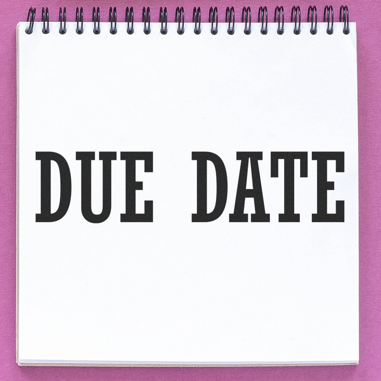 A notebook with DUE DATE stamped in bold black letters using the Large Pre-Inked Due Date Stamp, placed on a pink background.