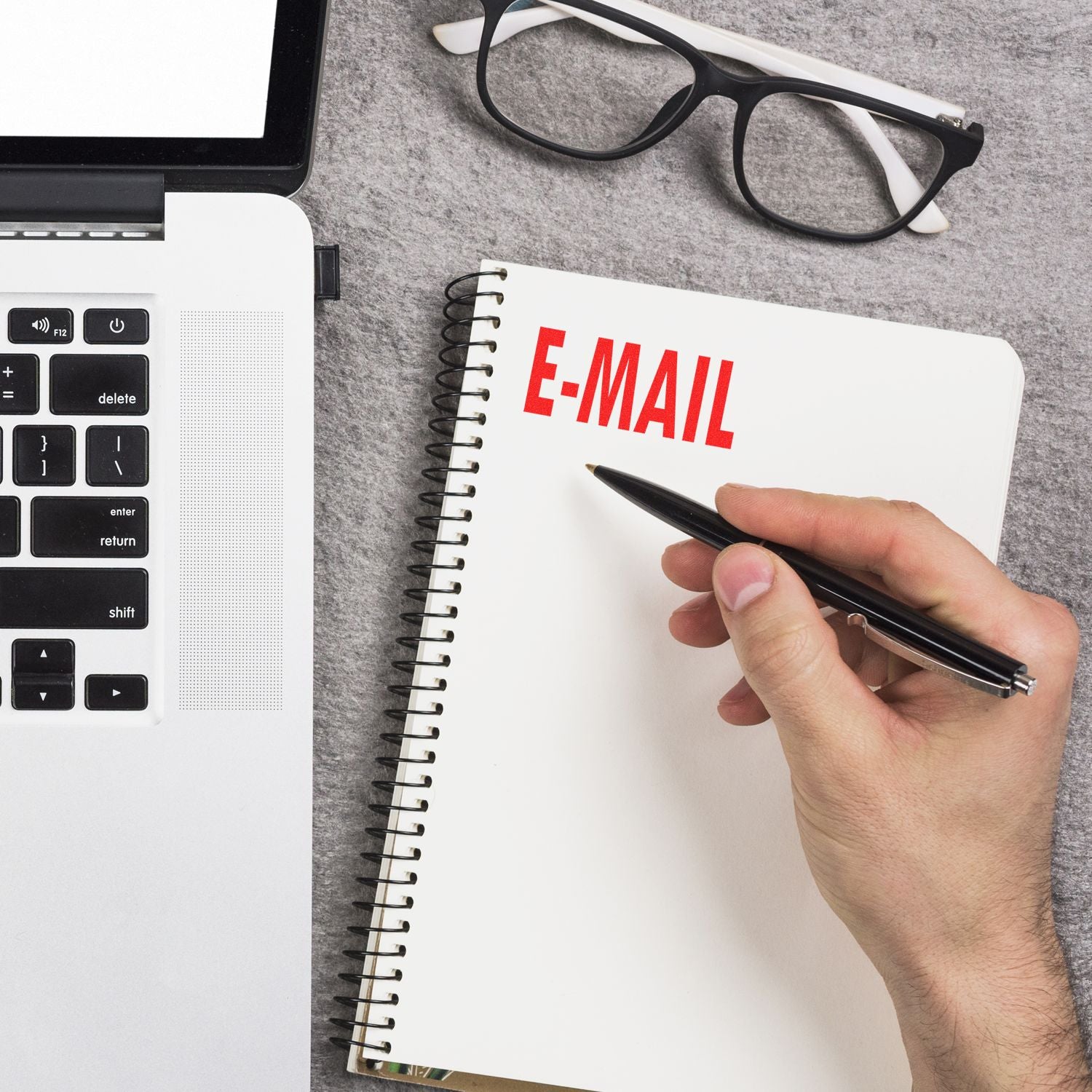 Hand using Self Inking E Mail Stamp on a notebook next to a laptop and glasses on a gray surface.