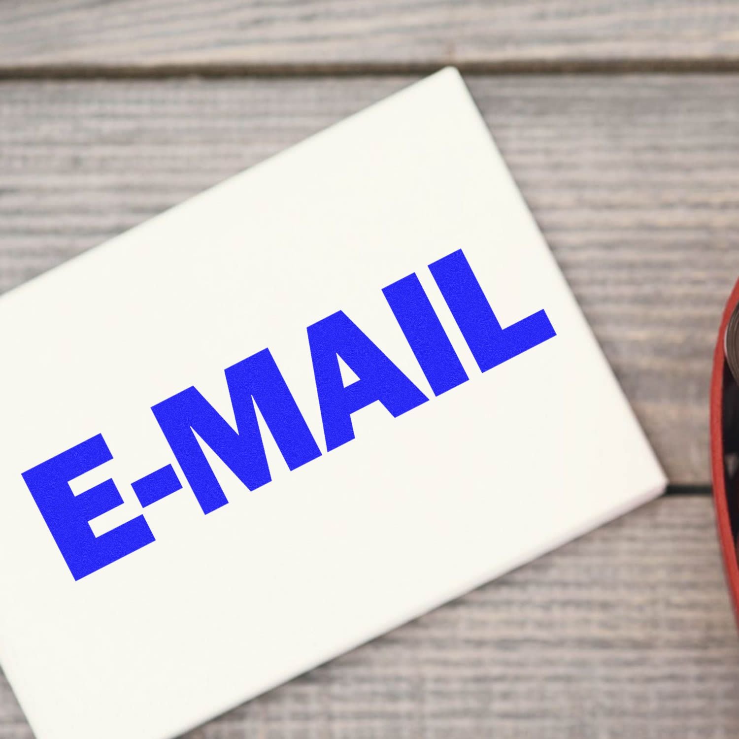 Large Self Inking E-Mail Stamp in use, stamping the word E-MAIL in bold blue letters on a white envelope on a wooden surface.