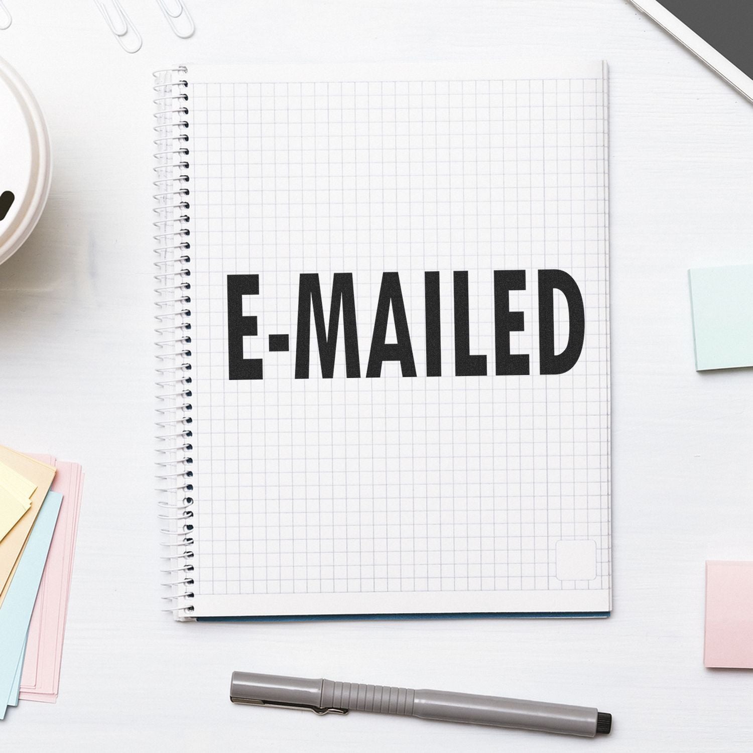 E Mailed Rubber Stamp used on a spiral notebook with grid paper, surrounded by sticky notes, a pen, and office supplies.