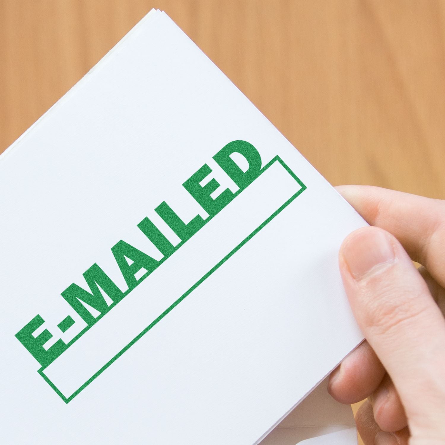 Person holding a document stamped with E-MAILED using a Slim Pre-Inked E-mailed with Date Box Stamp, on a wooden background.