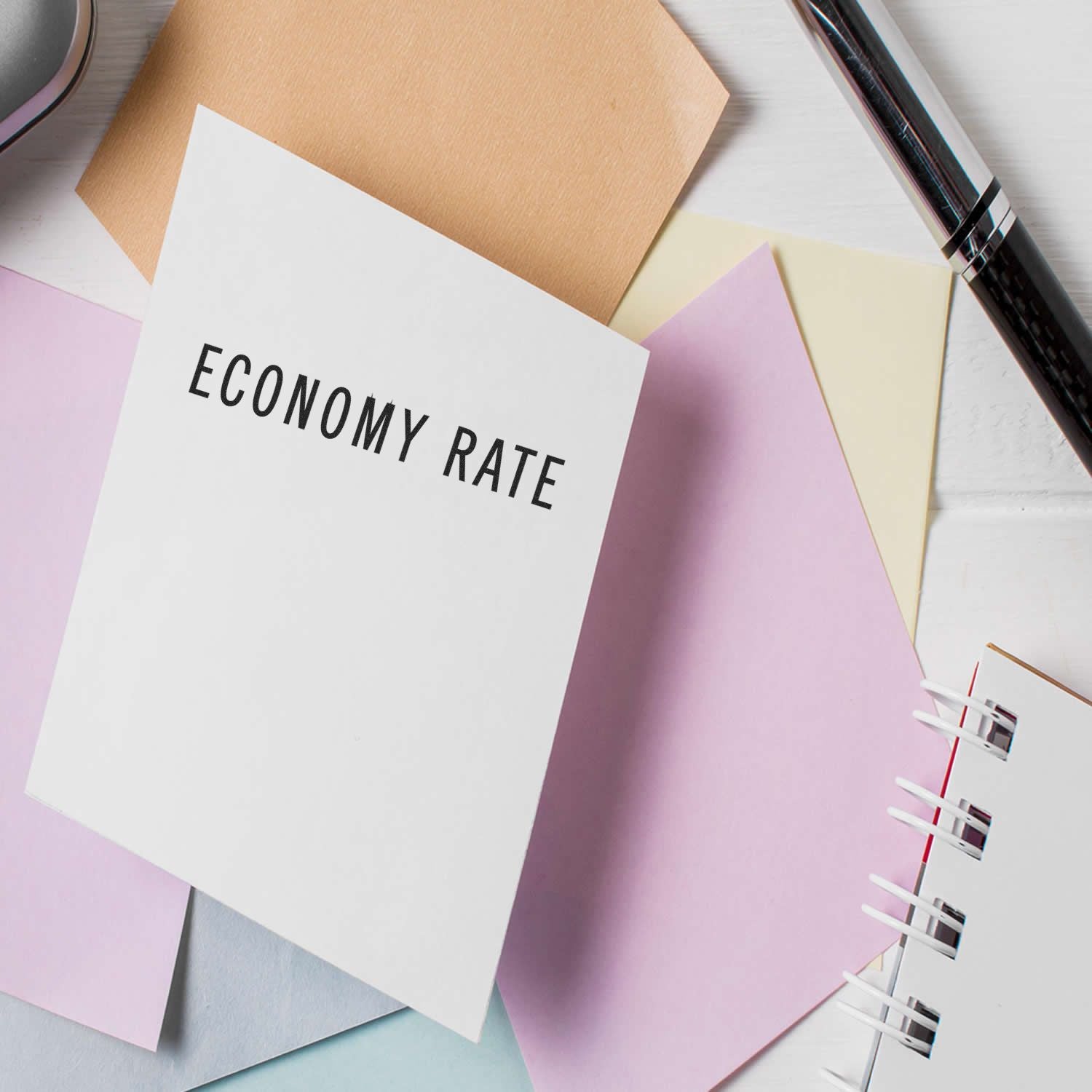 Large Economy Rate Rubber Stamp used on a white card, surrounded by pastel-colored papers and a pen on a white desk.