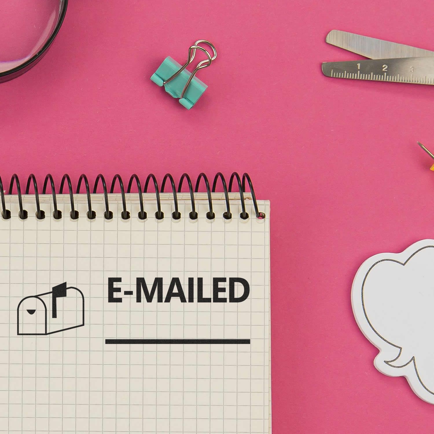 Large Self Inking Emailed with Mailbox Stamp used on a notepad, surrounded by office supplies on a pink background.