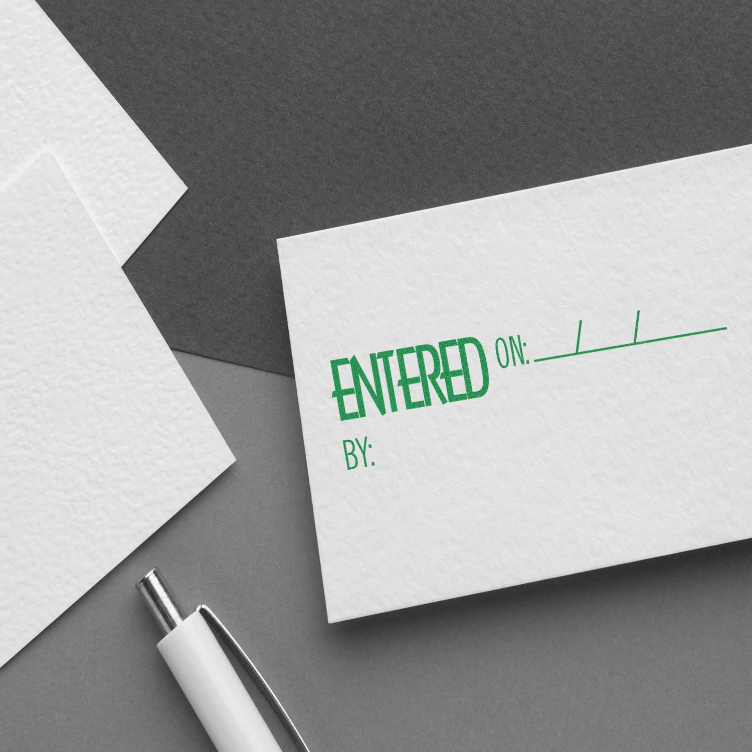 Entered On Rubber Stamp used on a white card with spaces for date and initials, placed on a gray surface next to a pen and other cards.