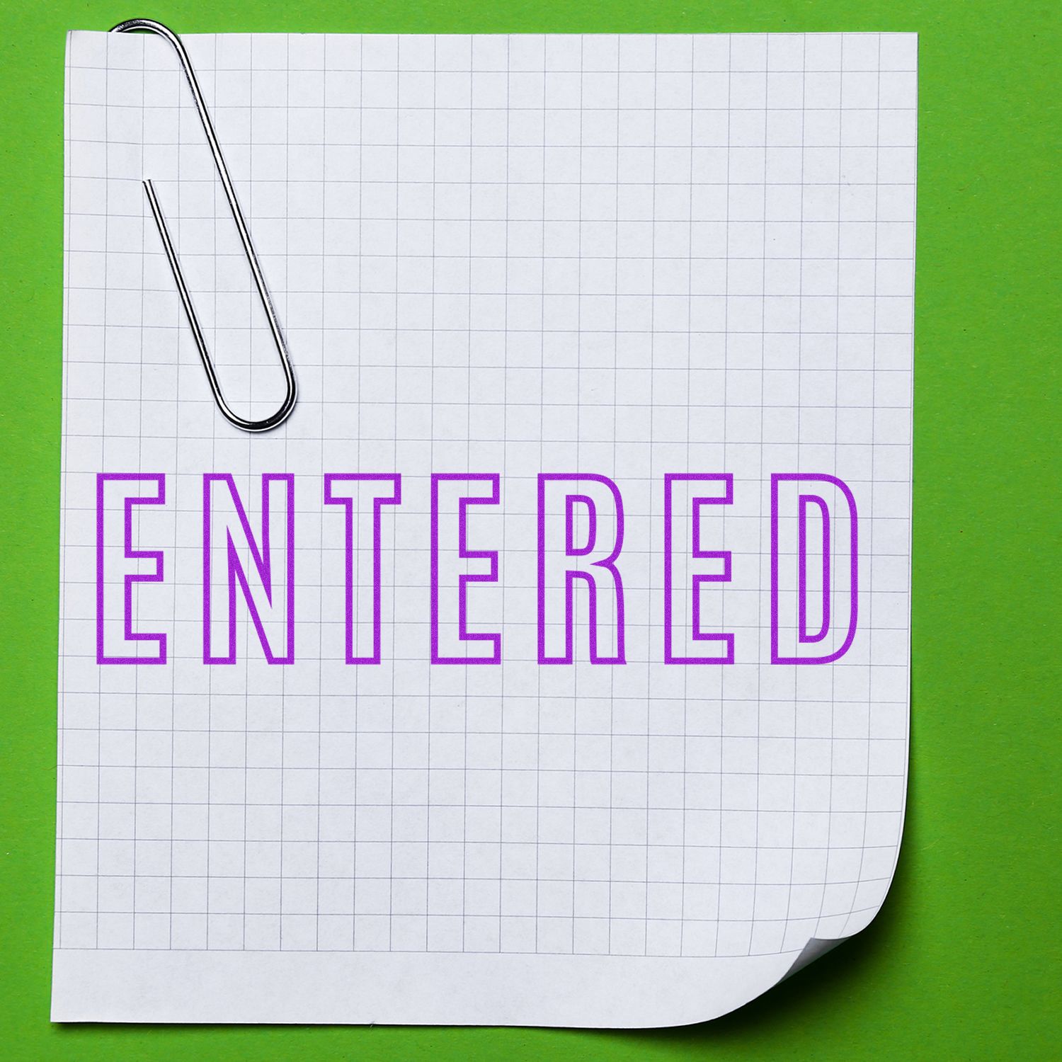 Large Self Inking Entered Outline Stamp in purple ink on a grid paper with a paperclip, placed on a green background.